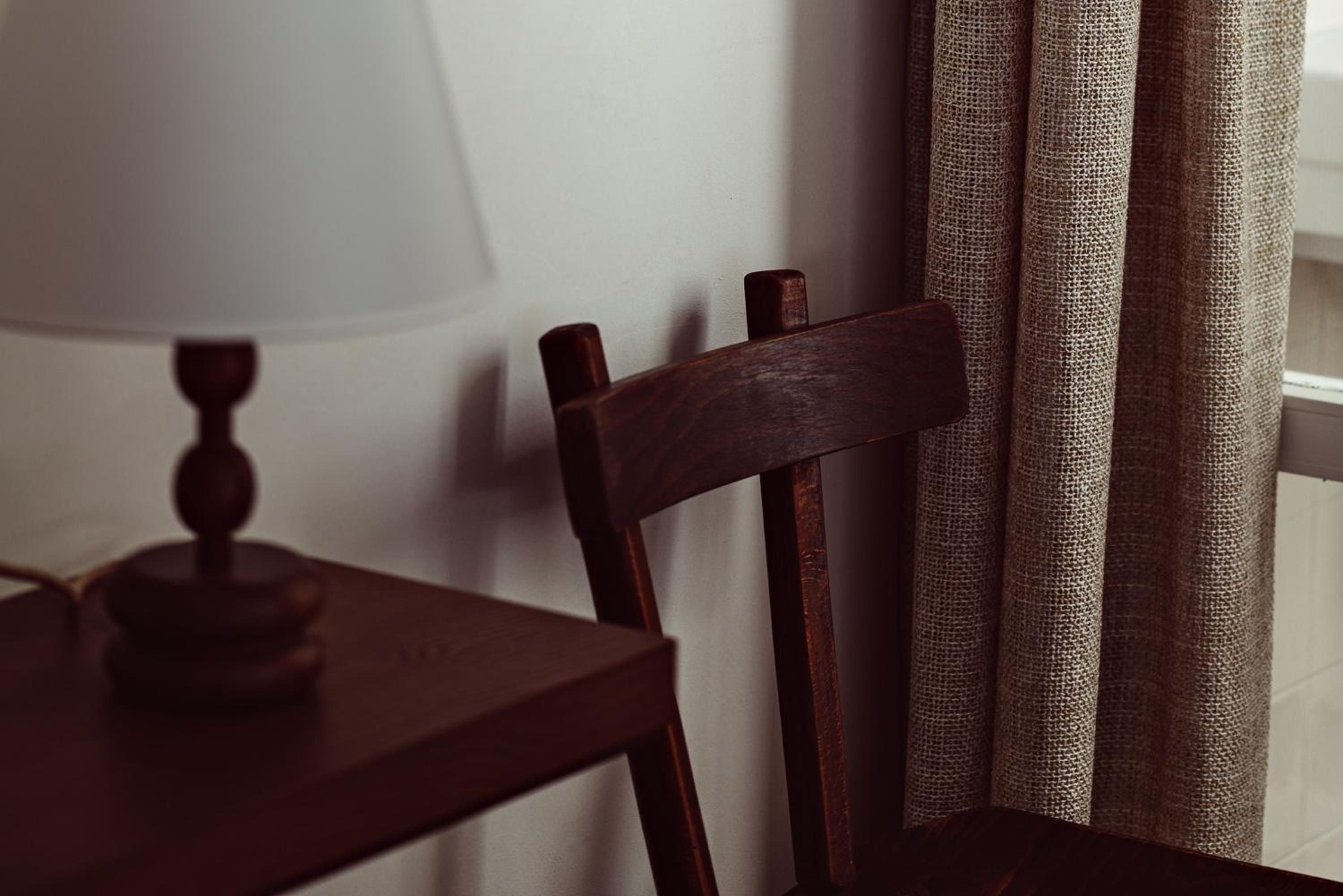 Rich walnut furniture and natural linen curtains create an intimate corner where warm afternoon light filters through, casting gentle shadows across handcrafted wood grain.