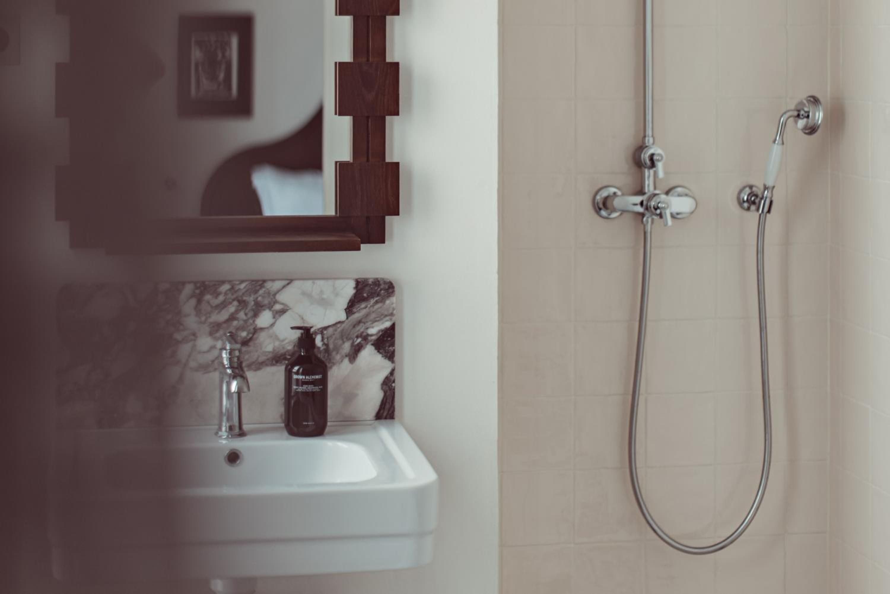 Marble veining and warm wood shelving create an intimate bathing sanctuary, where chrome fixtures gleam against soft neutral tones in this thoughtfully designed ensuite.