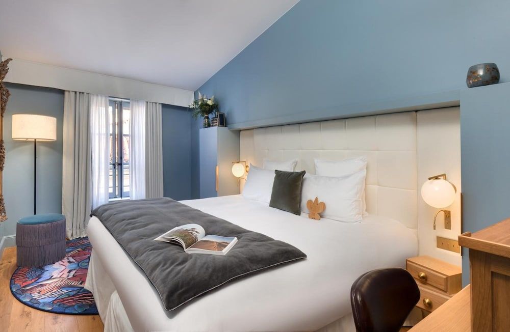 Soft blue walls and warm brass sconces create an intimate cocoon, while crisp white linens invite restful slumber in this thoughtfully designed guest room.