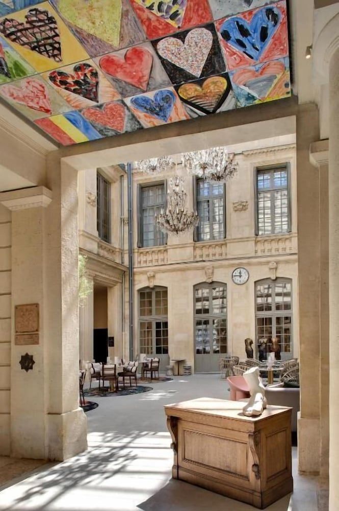 Colorful heart-shaped artwork crowns the grand limestone courtyard, where classical chandeliers cast elegant shadows across honey-toned stone and intimate seating areas.