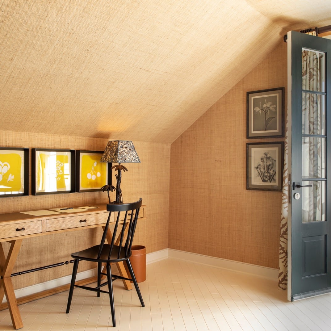 Woven grasscloth walls embrace this attic study, where golden light filters through geometric windows and botanical prints create an intimate creative sanctuary.