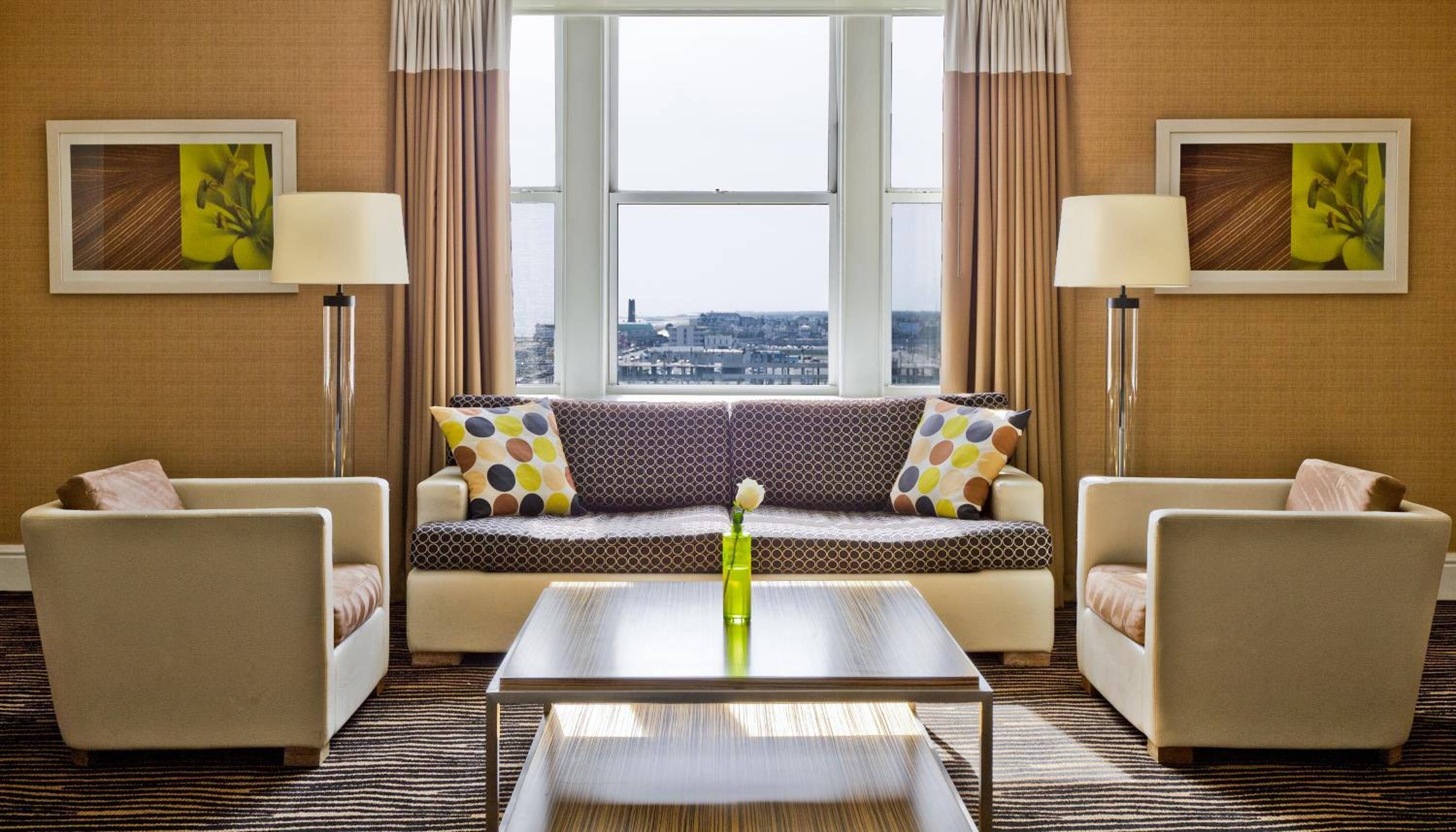 Sunlight streams through floor-to-ceiling windows, illuminating geometric patterns and warm wood tones in this sophisticated living space with sweeping city views.