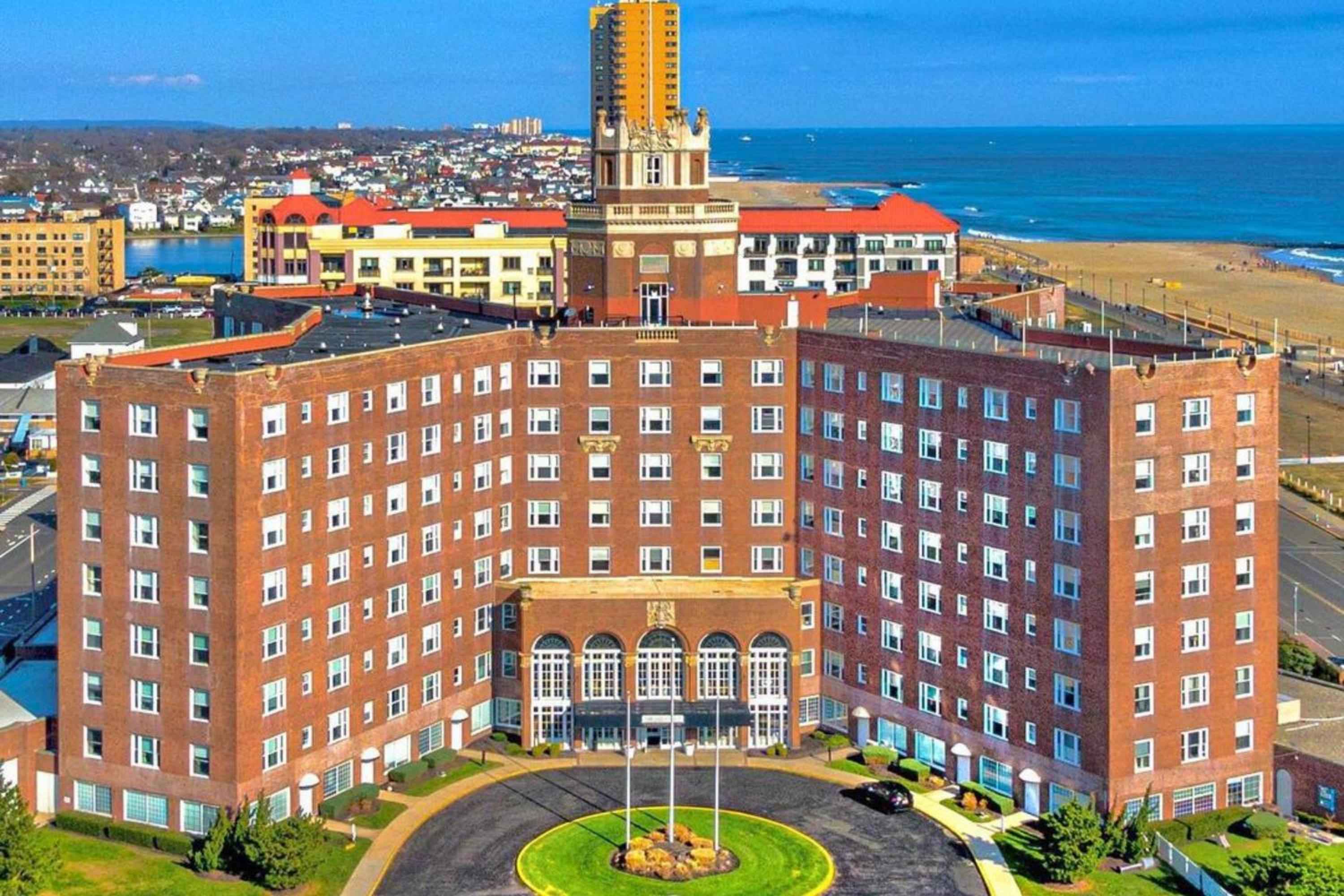 Brick wings embrace a grand circular drive while Atlantic breeze carries salt air past this stately seaside landmark, its commanding presence anchoring the vibrant boardwalk beyond.