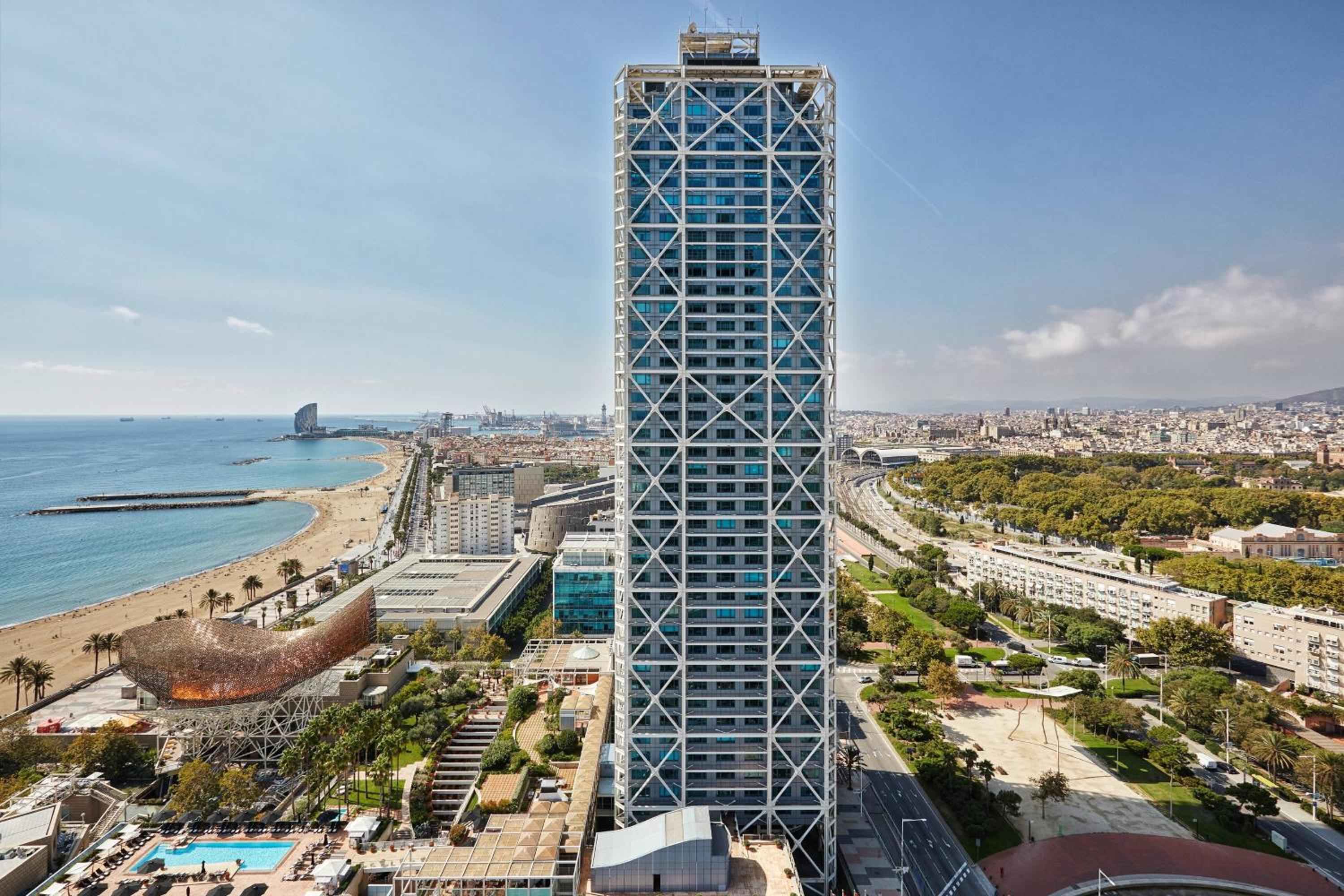 Hotel Arts' striking geometric tower rises majestically above Barcelona's golden coastline, its diamond-patterned facade catching Mediterranean light while overlooking the bustling Barceloneta beach below.