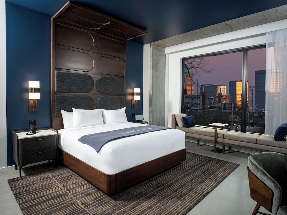 Floor-to-ceiling windows frame the city's golden hour glow while rich navy walls and walnut furnishings create an intimate urban sanctuary high above the bustling streets.