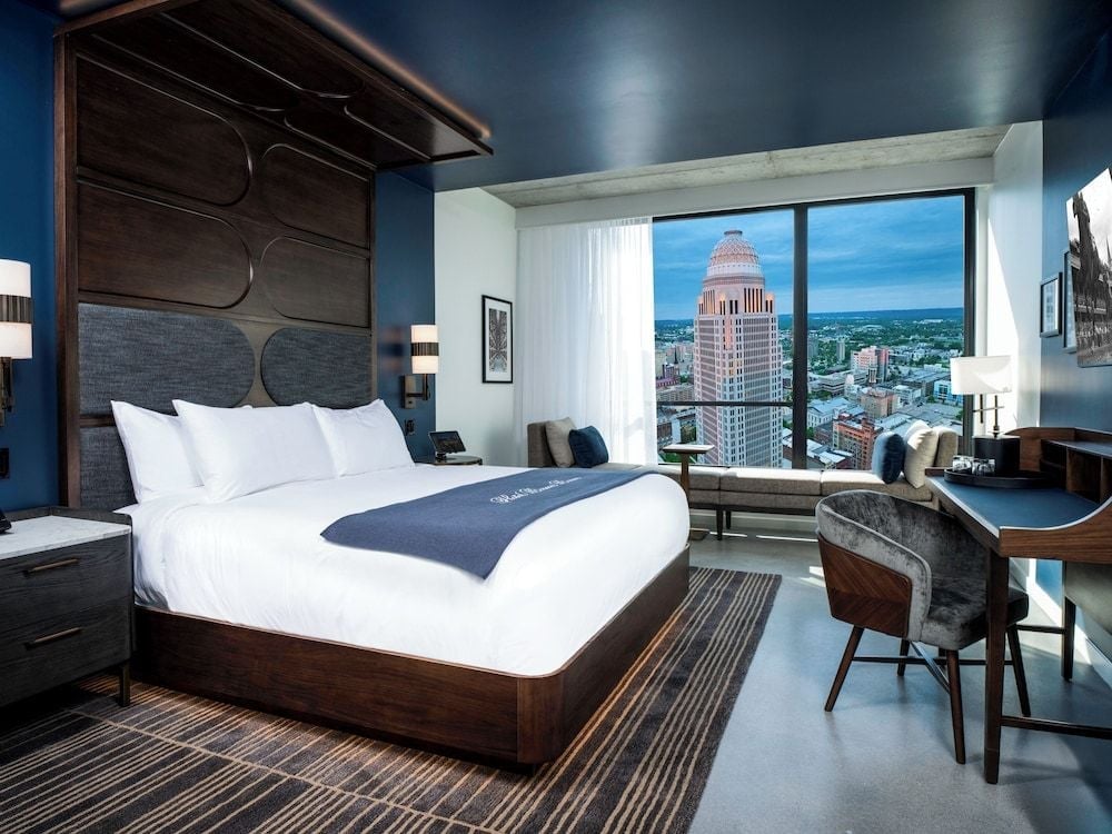 Floor-to-ceiling windows frame the Louisville skyline from this sophisticated guest room, where navy walls and rich walnut furnishings create an intimate urban retreat.