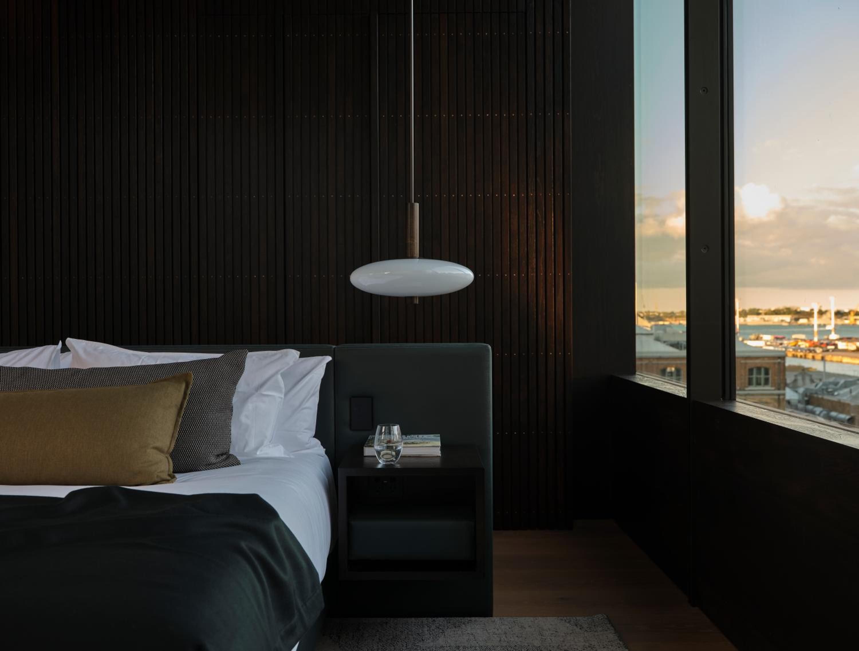 Floor-to-ceiling windows frame Auckland's harbor while charcoal timber slats create intimate shadows, transforming this minimalist suite into a sophisticated urban sanctuary.