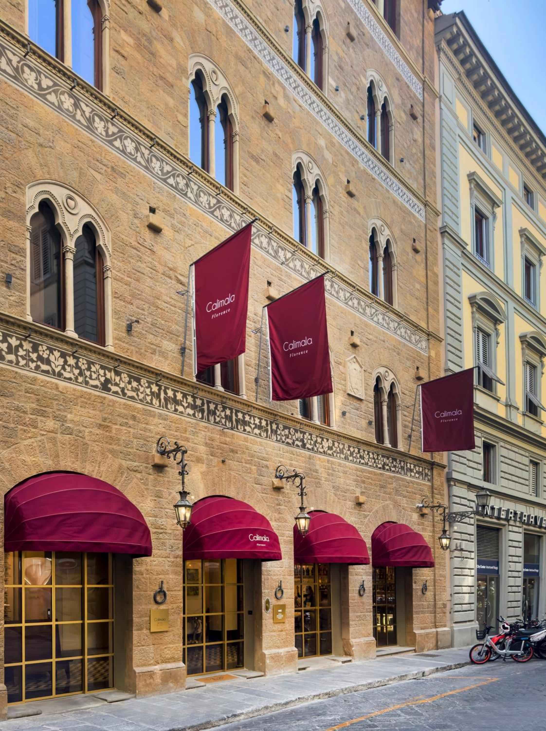 Burgundy awnings cast shadows over medieval stone arches where centuries-old Florentine craftsmanship meets modern luxury along cobblestone streets.