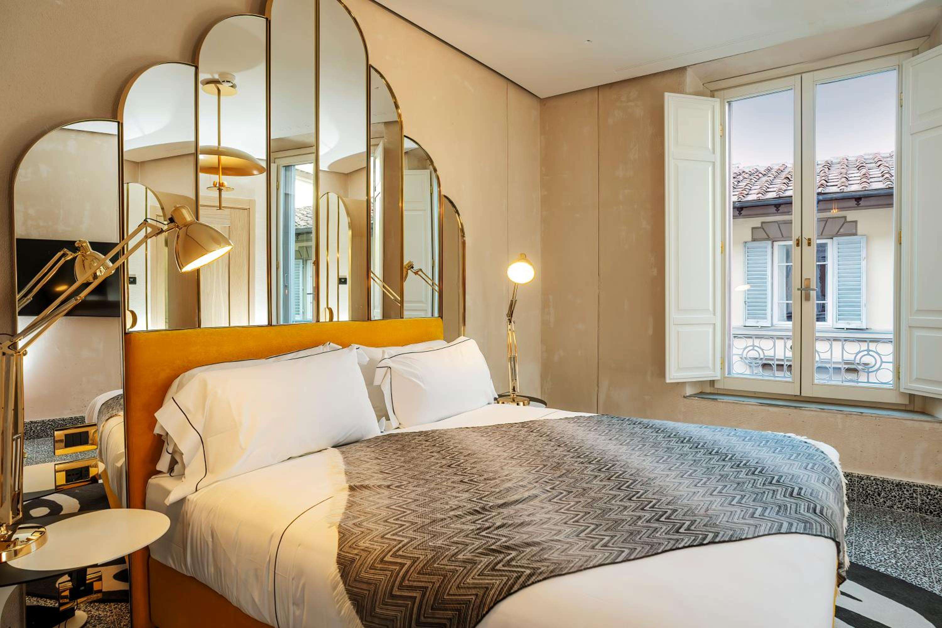 Golden brass task lamps and curved mirror panels create intimate warmth in this thoughtfully designed guest room, where chevron throws complement peachy terracotta walls.