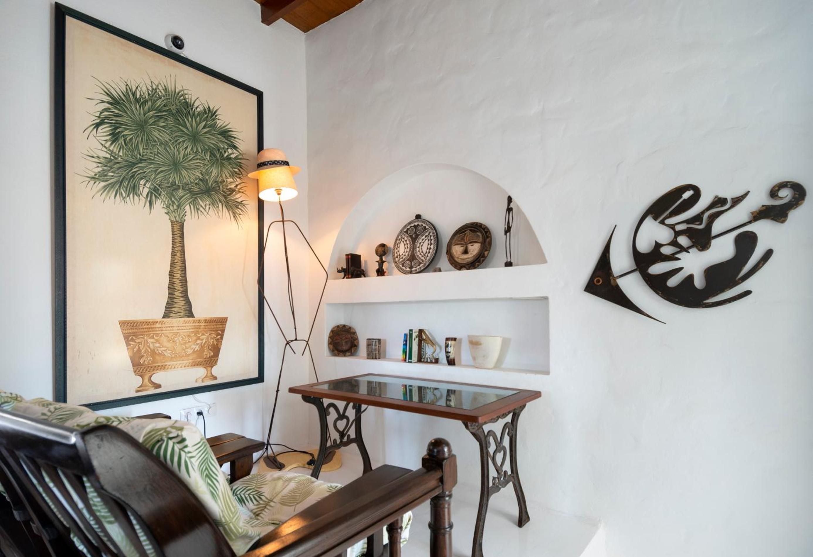 Whitewashed alcoves display curated artifacts while a vintage palm print and ornate writing desk create an intimate corner that whispers of old-world Mediterranean charm.
