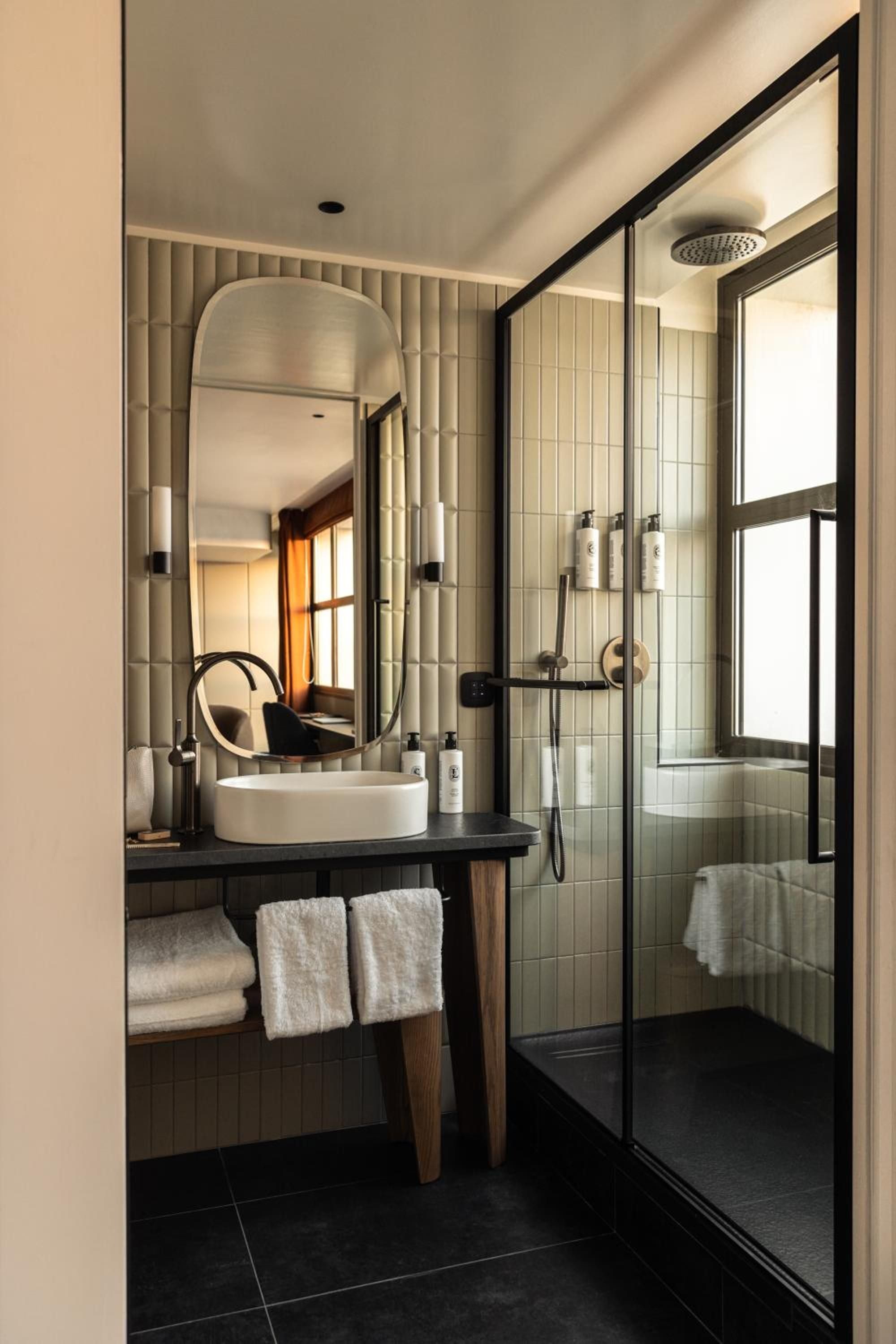 Vertical tiles in warm cream hues create textural intrigue, while black fixtures and sleek glass shower enclosures bring modern sophistication to this intimate sanctuary.