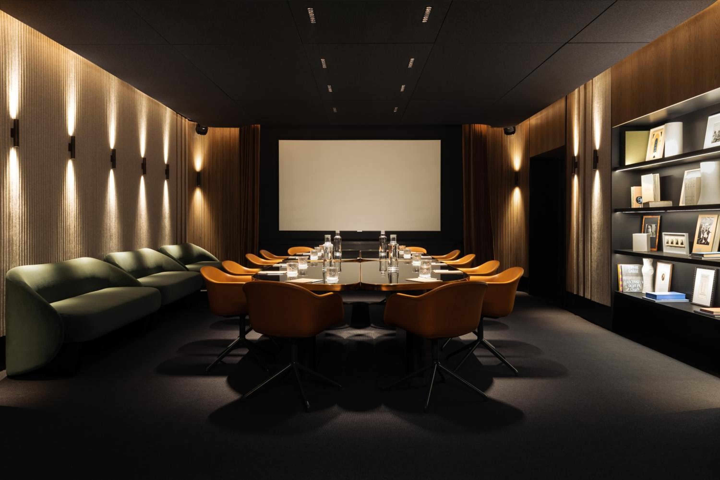 Warm wood paneling and amber lighting create an intimate boardroom sanctuary, where cognac-colored leather chairs gather around polished tables beneath dramatic black ceilings.
