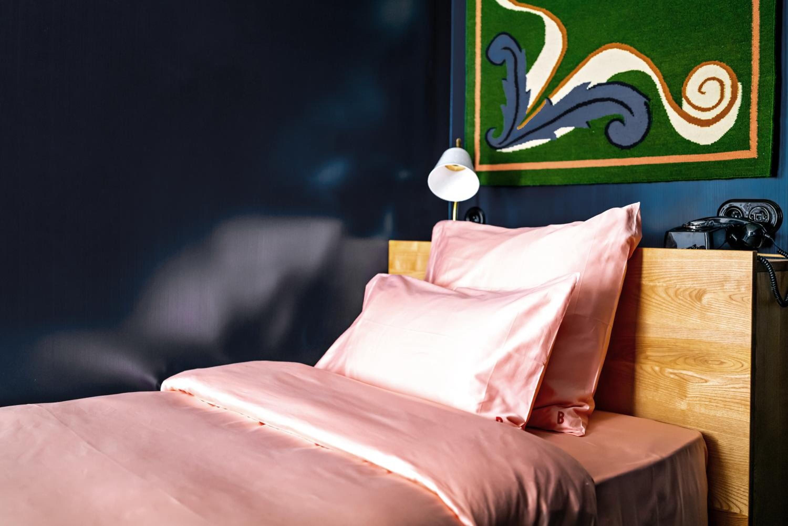 Coral-hued linens catch morning light against midnight blue walls, while a whimsical green artwork adds unexpected charm to this intimate sleeping sanctuary.