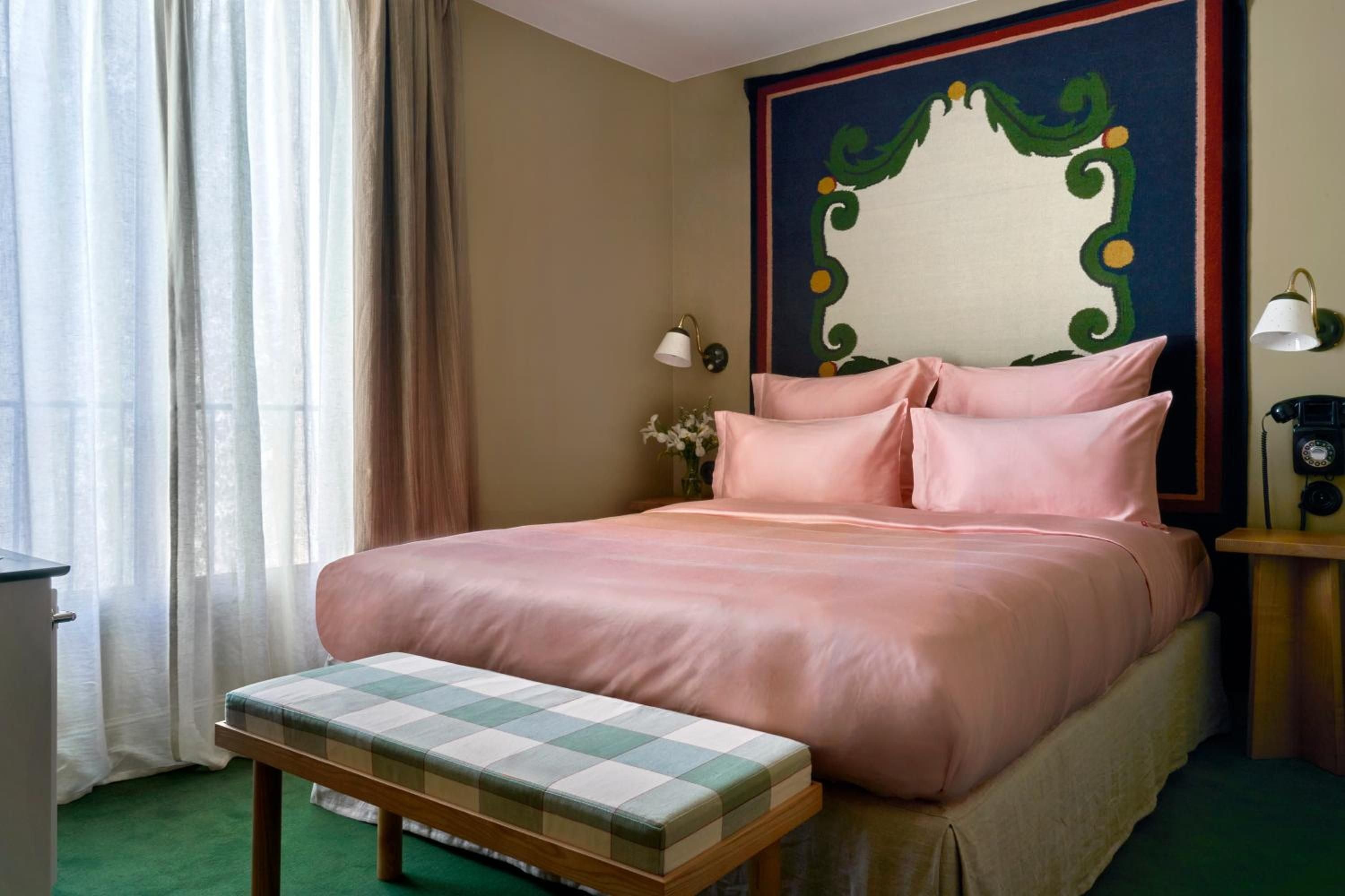 Blush-toned linens complement the hand-painted headboard's whimsical green flourishes, while brass sconces cast warm light across this thoughtfully appointed guest room.