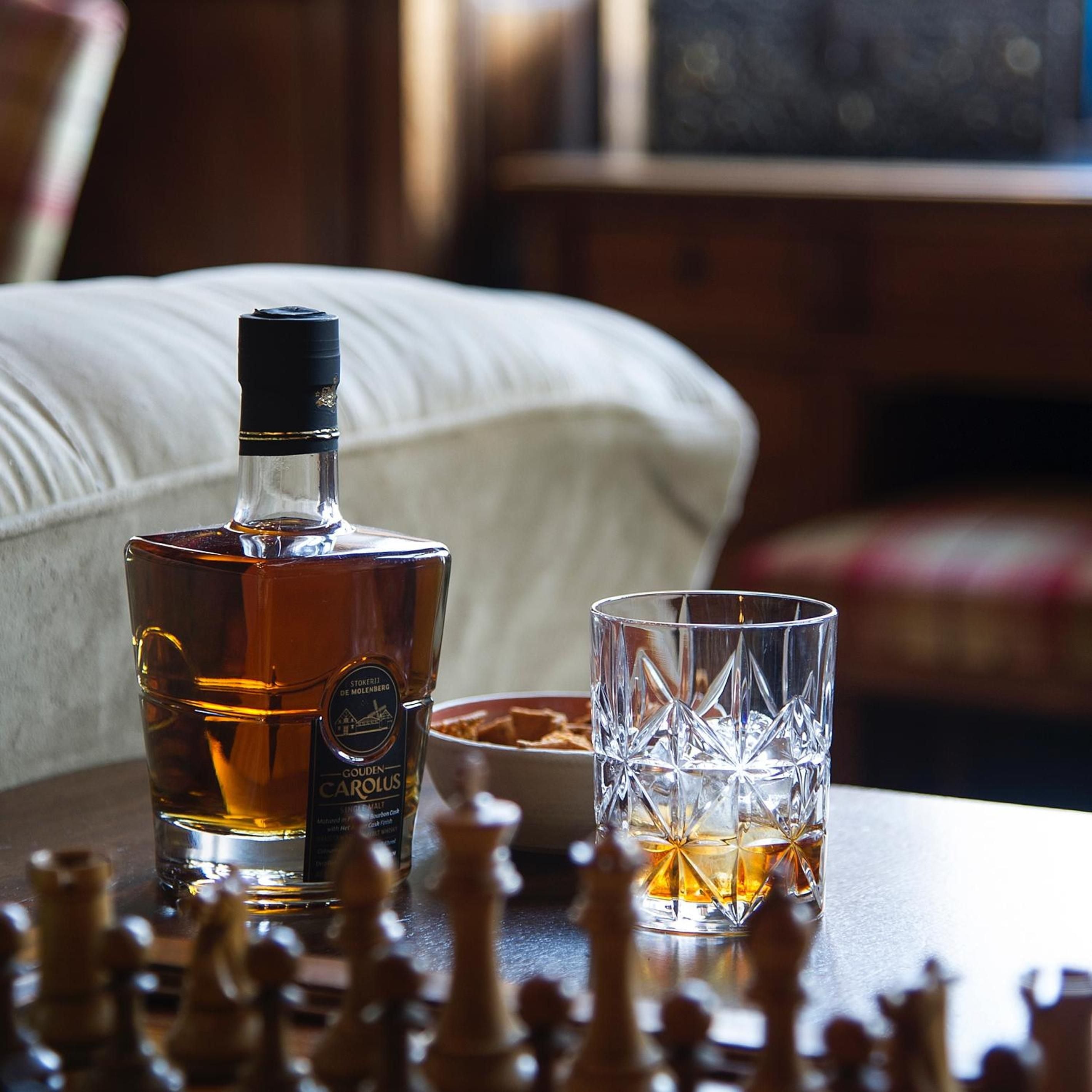 Golden whiskey catches afternoon light in a crystal tumbler, while chess pieces await the next move in this intimate corner of refined indulgence.