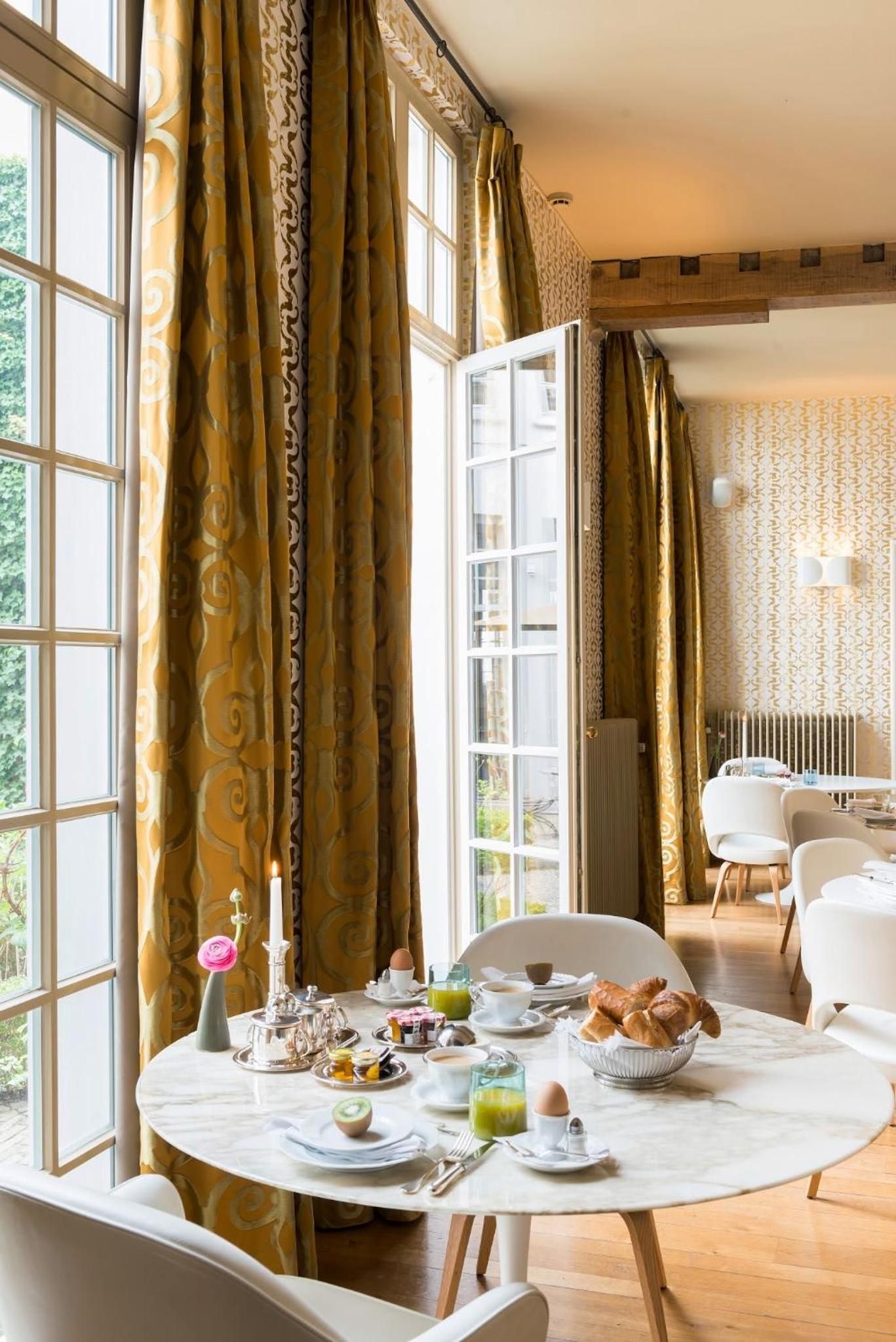 Golden baroque curtains frame tall windows where morning light illuminates an intimate breakfast spread, complete with fresh pastries and delicate china on marble tables.