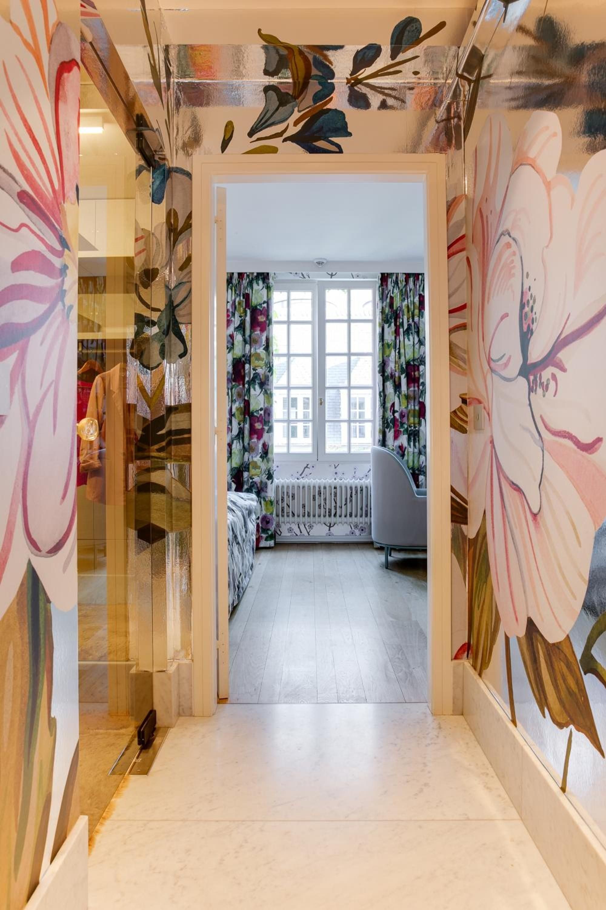 Vibrant botanical murals transform this intimate hallway into an artistic passage, where hand-painted florals dance across mirrored surfaces toward a sun-drenched bedroom beyond.