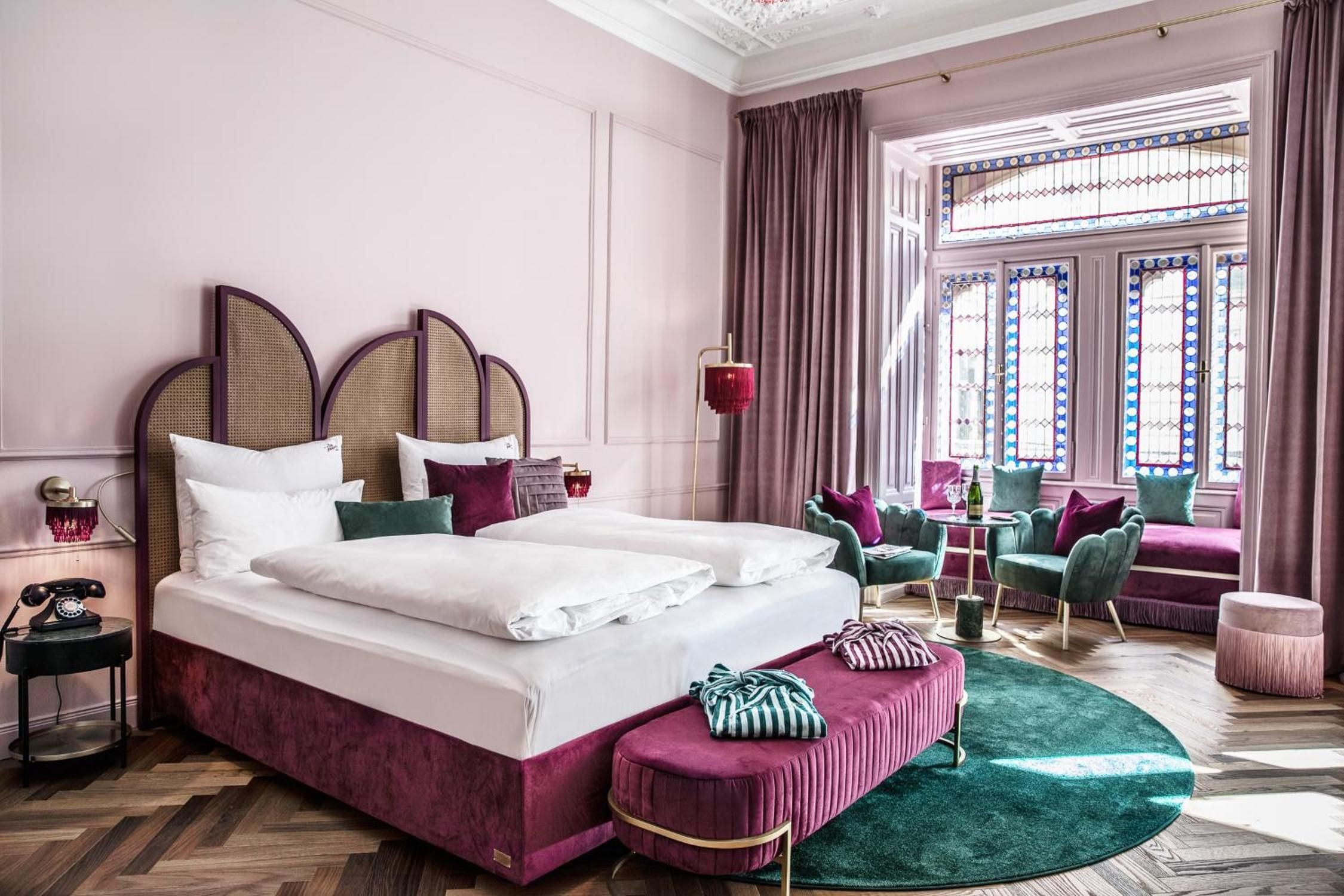 Velvet burgundy and emerald tones create an opulent sanctuary where cane headboards meet jewel-toned seating beneath ornate stained glass windows.