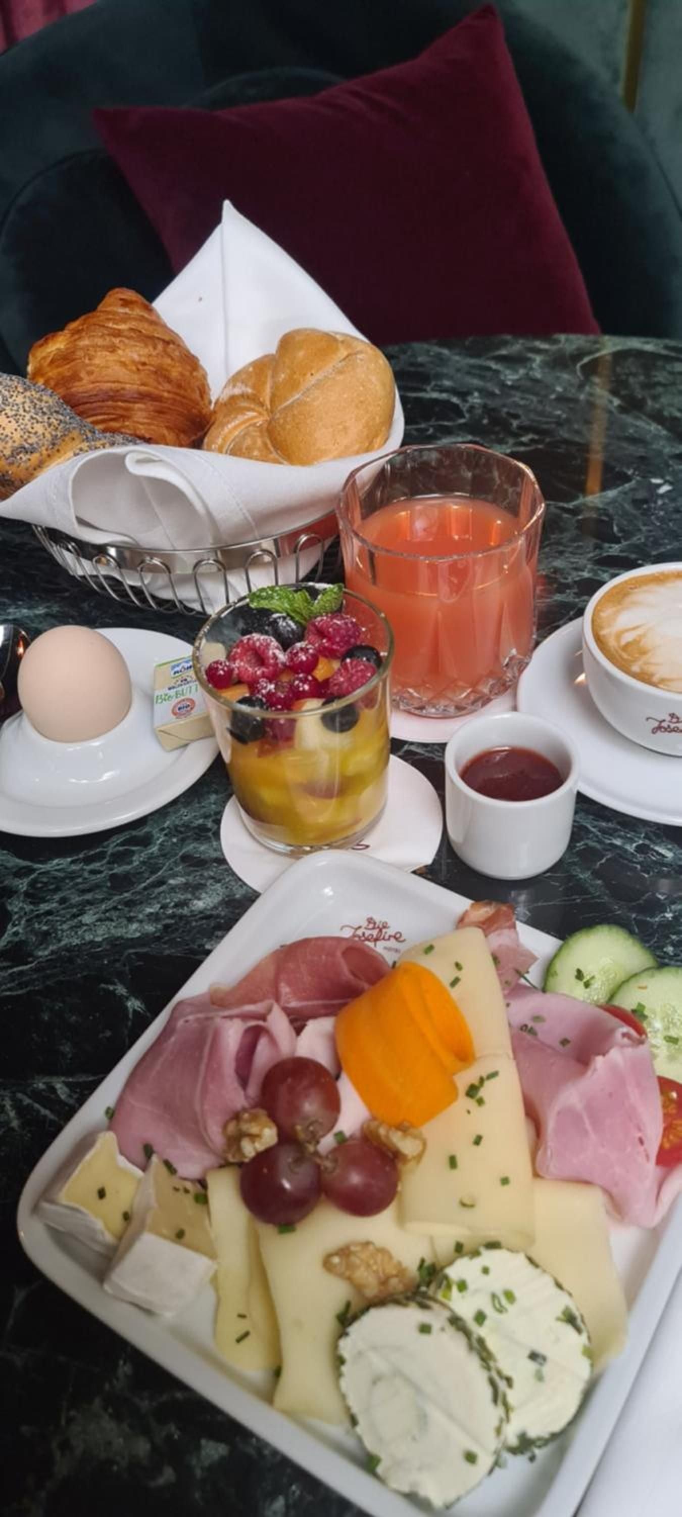 Continental breakfast spreads across marble tables with house-made pastries, artisanal cheeses, and freshly squeezed juice creating an intimate morning ritual in velvet-cushioned comfort.