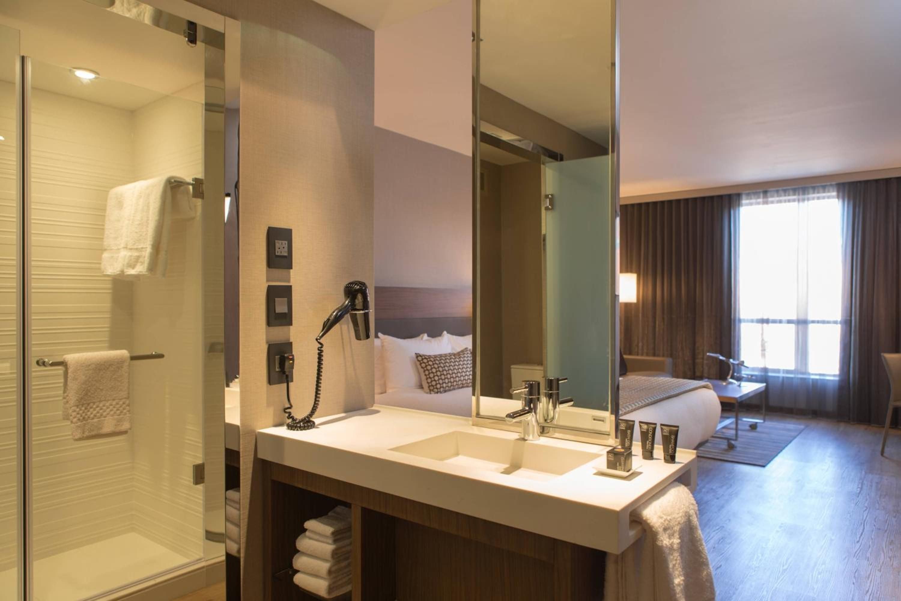 Glass-walled bathrooms blur boundaries between sleeping and bathing spaces, while warm wood vanities and sleek fixtures create an intimate yet airy sanctuary above the city.
