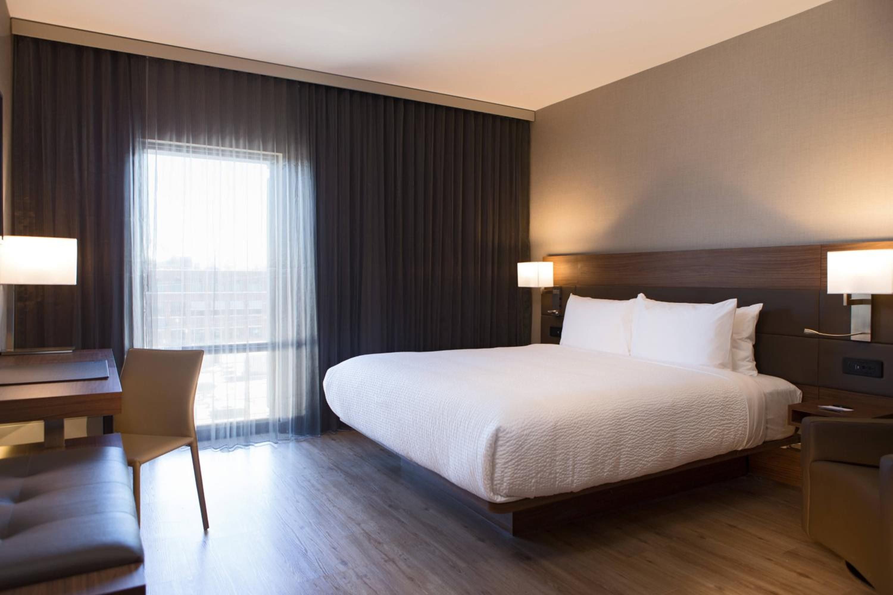 Warm wood tones and clean lines define guest rooms where floor-to-ceiling windows frame city views, creating an urban sanctuary with sophisticated midwestern comfort.