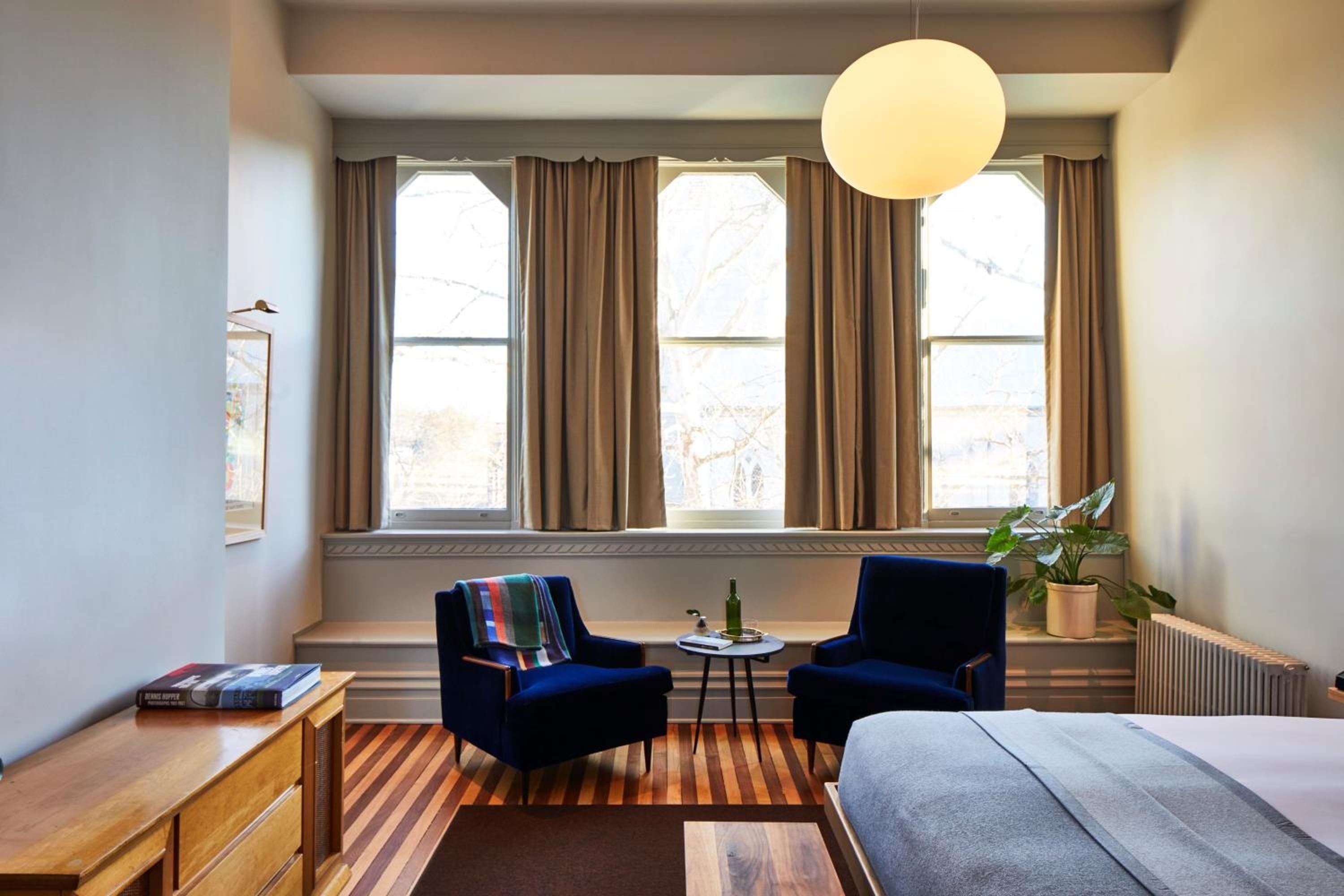 Navy velvet chairs frame a window-lit reading nook where striped wool throws and warm wood tones create an inviting retreat above the bustling streets.