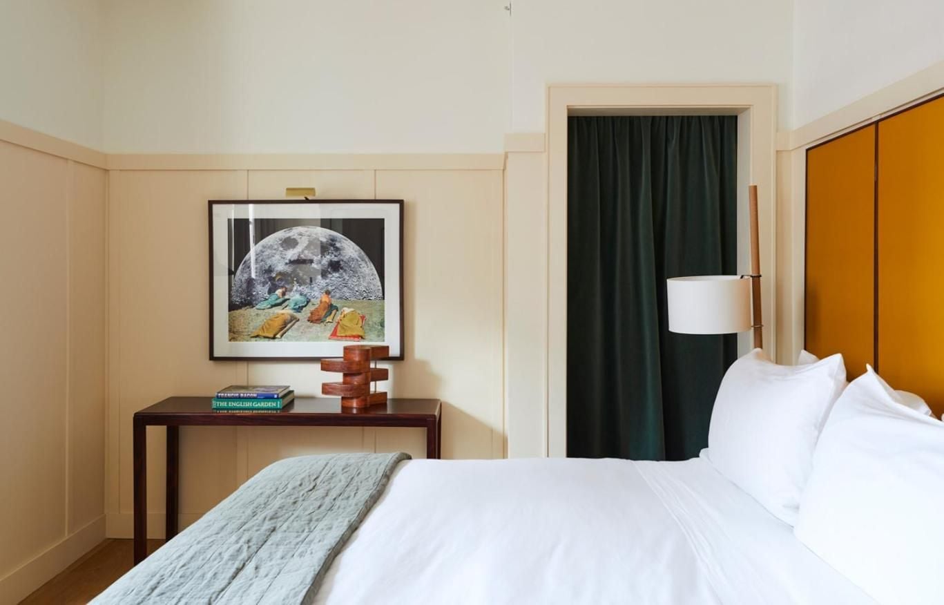 Crisp white linens meet warm wood paneling in thoughtfully appointed guest rooms, where moon-themed artwork and forest-green curtains create an intimate, residential feel.