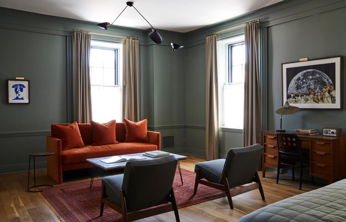 Sage-green paneling and burnt orange velvet create intimate sophistication in this corner suite, where mid-century chairs invite lingering over morning coffee and evening conversations.