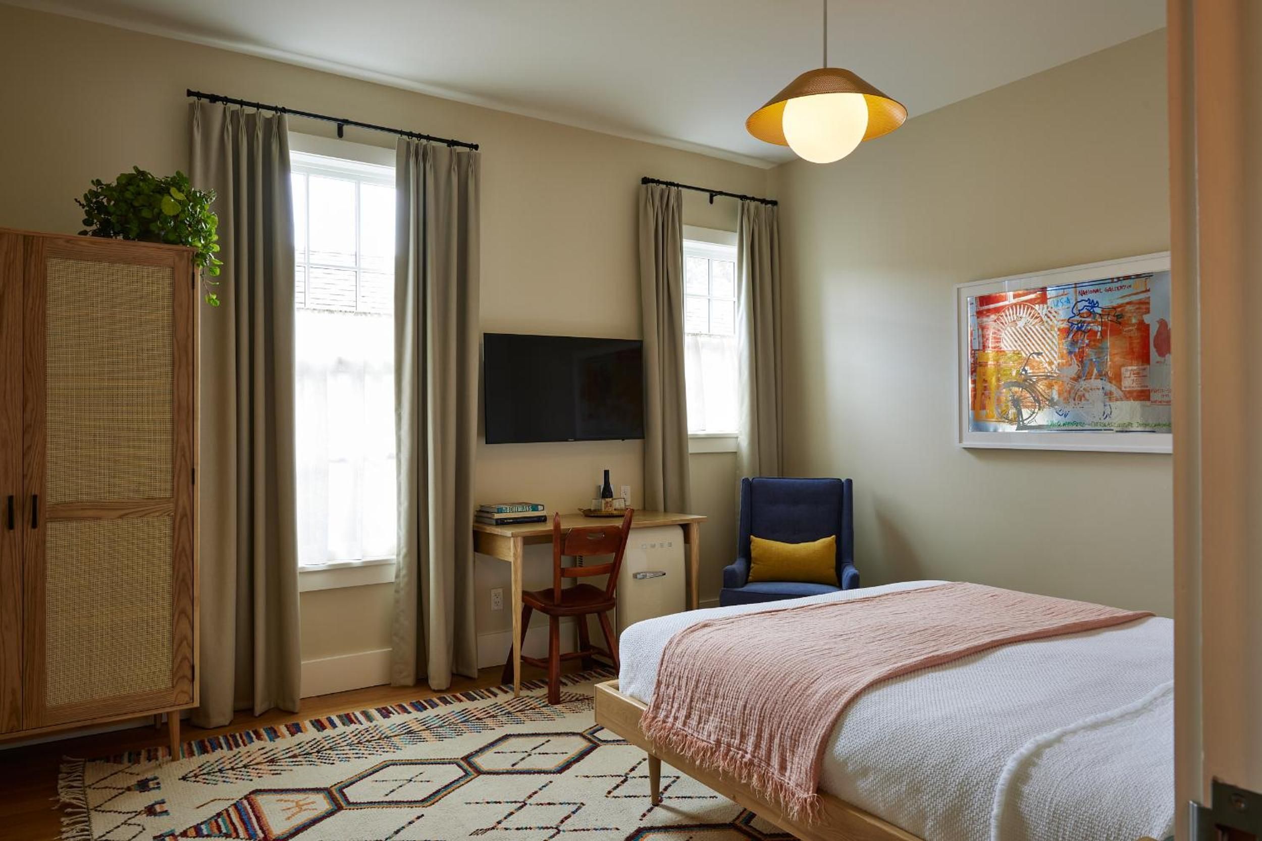 Mid-century warmth meets modern comfort in thoughtfully appointed guest rooms, where cane furniture, geometric rugs, and golden pendant lighting create an instantly welcoming retreat.