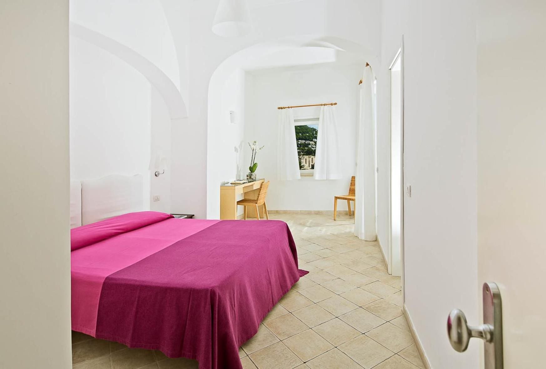 Whitewashed walls and traditional stone floors create a serene sanctuary, where vibrant fuchsia linens add a playful Mediterranean touch to minimalist elegance.