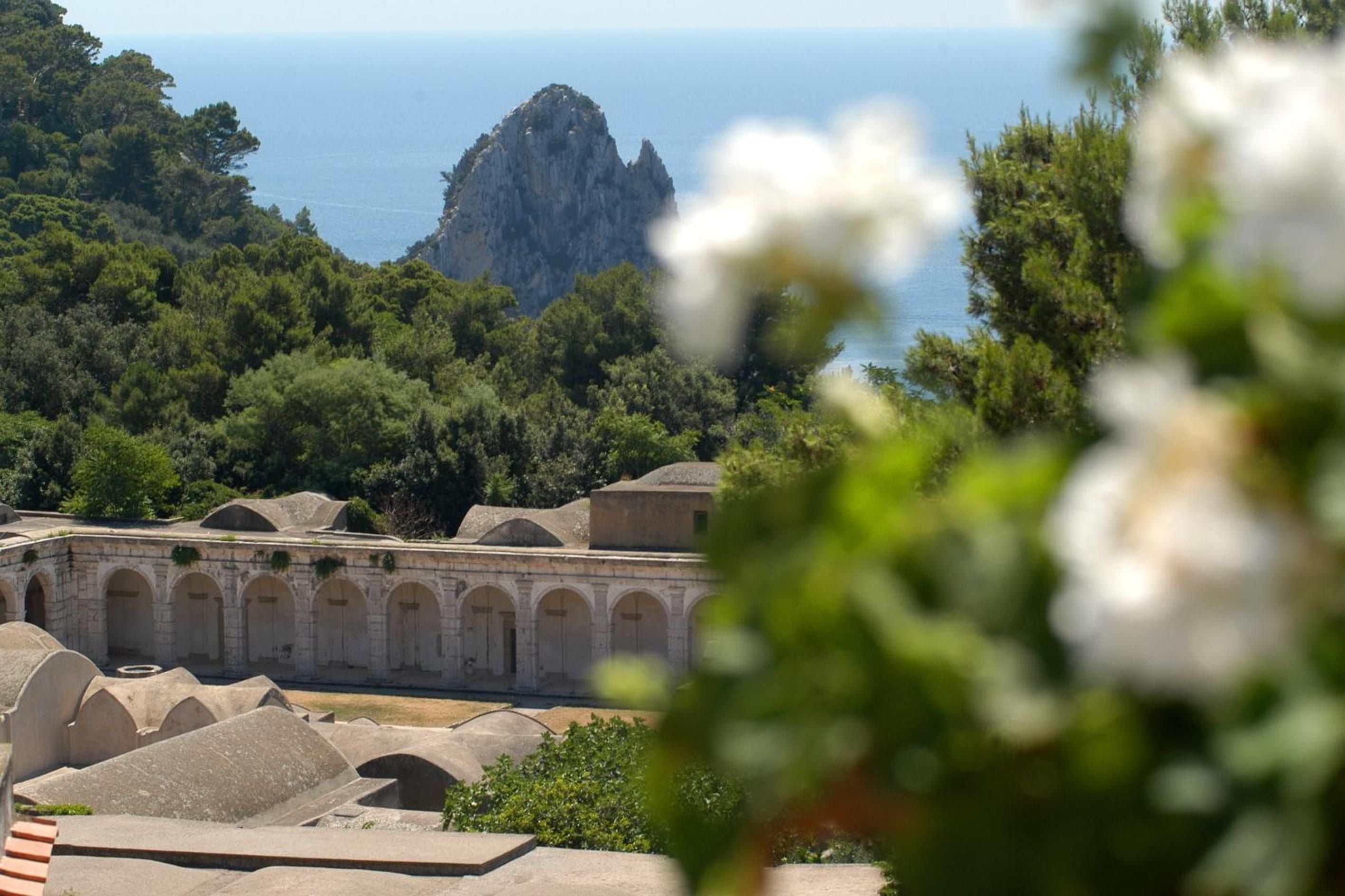 Ancient stone arches frame the dramatic limestone peaks beyond, while fragrant jasmine blooms soften the rustic Mediterranean architecture of this enchanting hillside retreat.