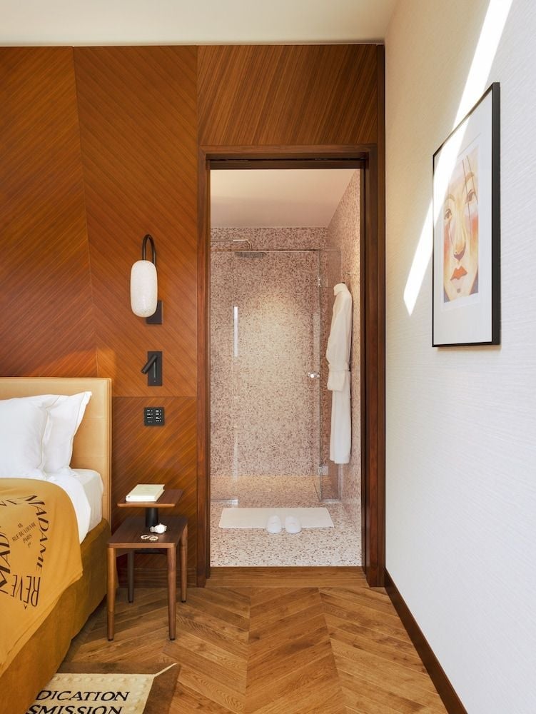 Warm walnut paneling creates an intimate cocoon, while the glass-walled shower beyond hints at the seamless blend of bedroom and bath in this thoughtfully designed space.