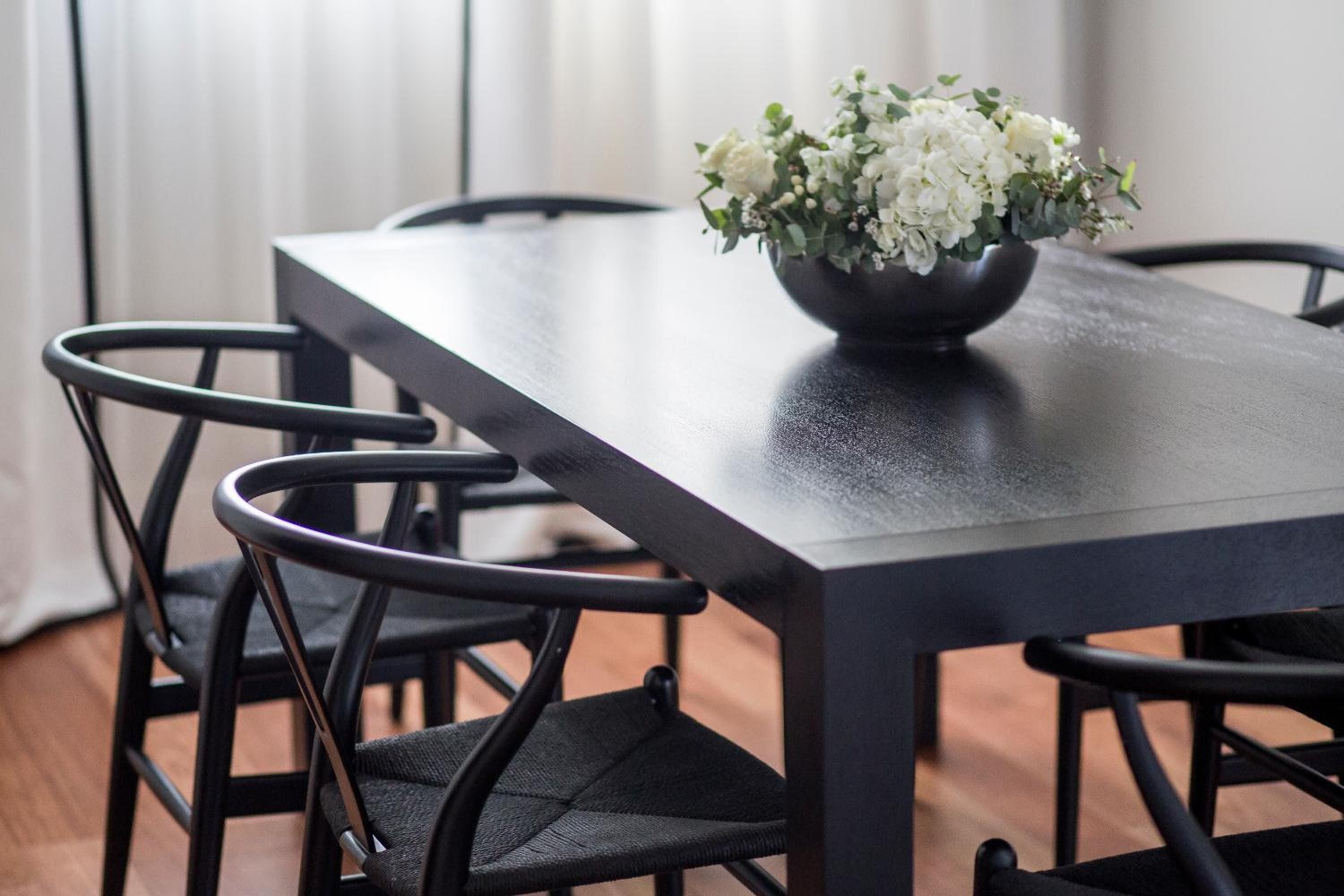 Sleek black dining chairs frame a polished table where fresh white blooms cast gentle shadows, creating an intimate corner for unhurried conversations over exceptional cuisine.