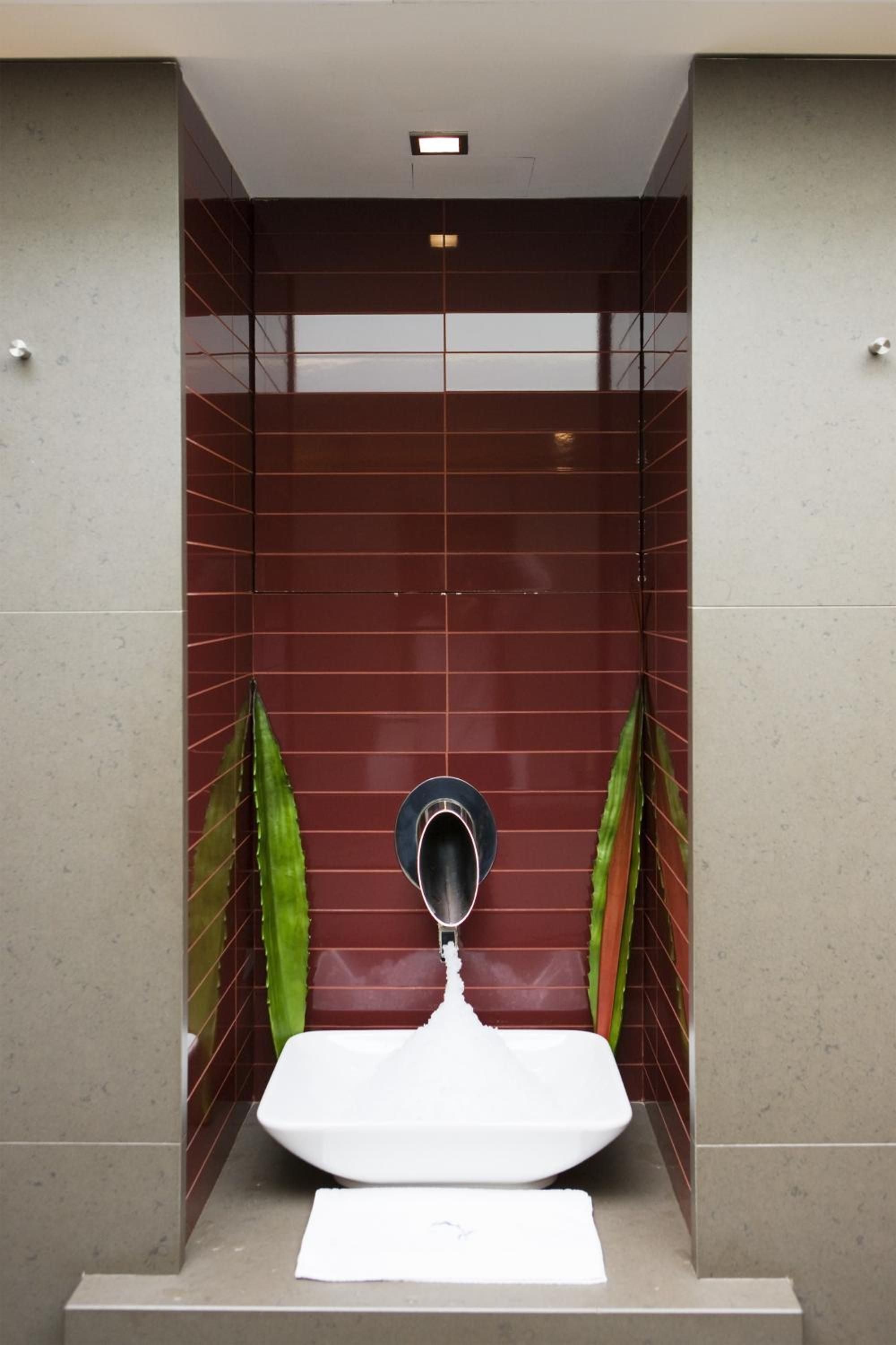 Burgundy tiles create a striking backdrop in this minimalist powder room, where sleek fixtures and vibrant green plants add contemporary sophistication to intimate spaces.