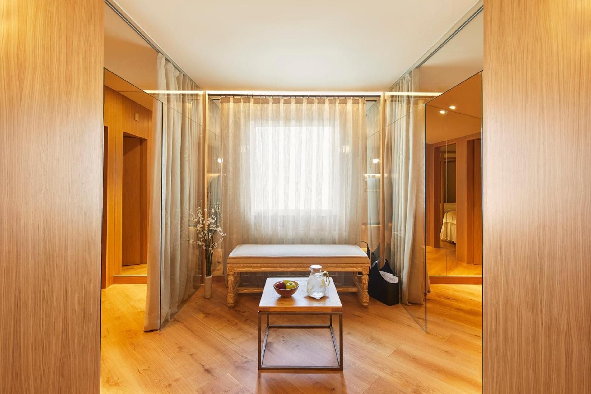 Warm wooden panels and gossamer curtains create an intimate sanctuary where natural light filters through sheer drapes, transforming treatments into pure tranquility.