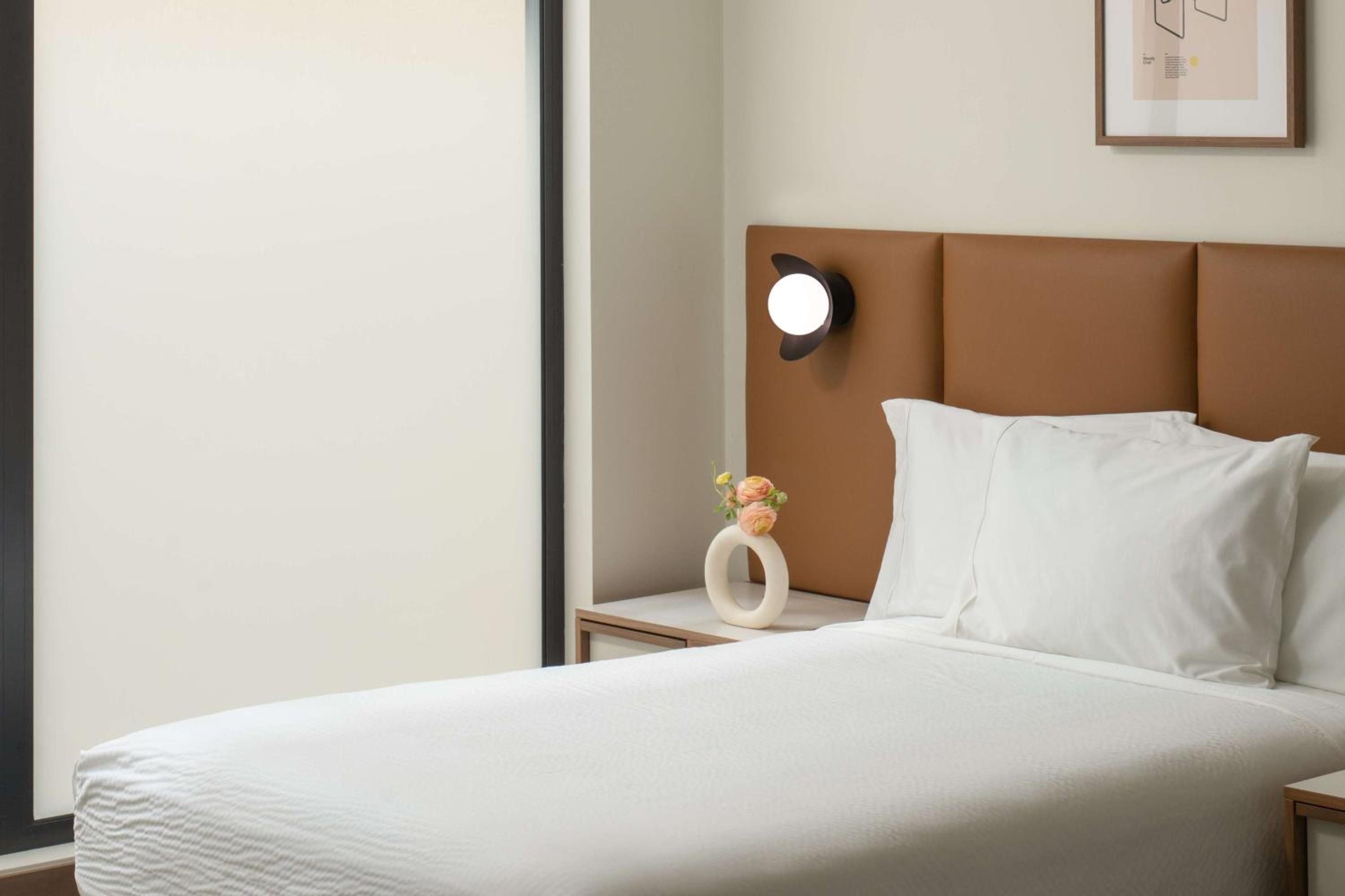 Crisp white linens meet warm cognac leather headboards, while sculptural sconces and delicate florals create an intimate, contemporary sanctuary that feels both polished and inviting.