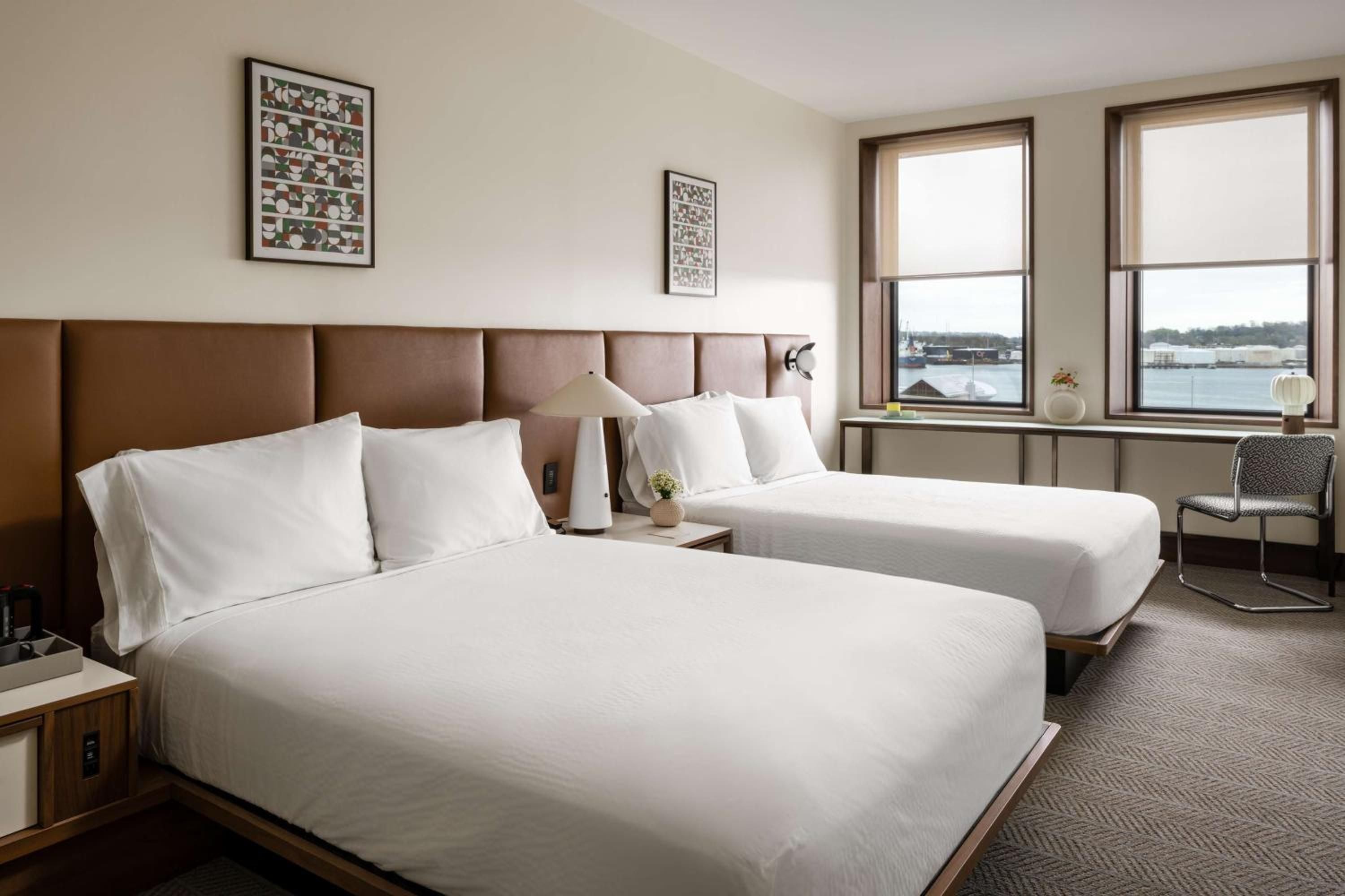 Two plush beds frame harbor views through oversized windows, while warm taupe headboards and geometric artwork create an inviting waterfront retreat.