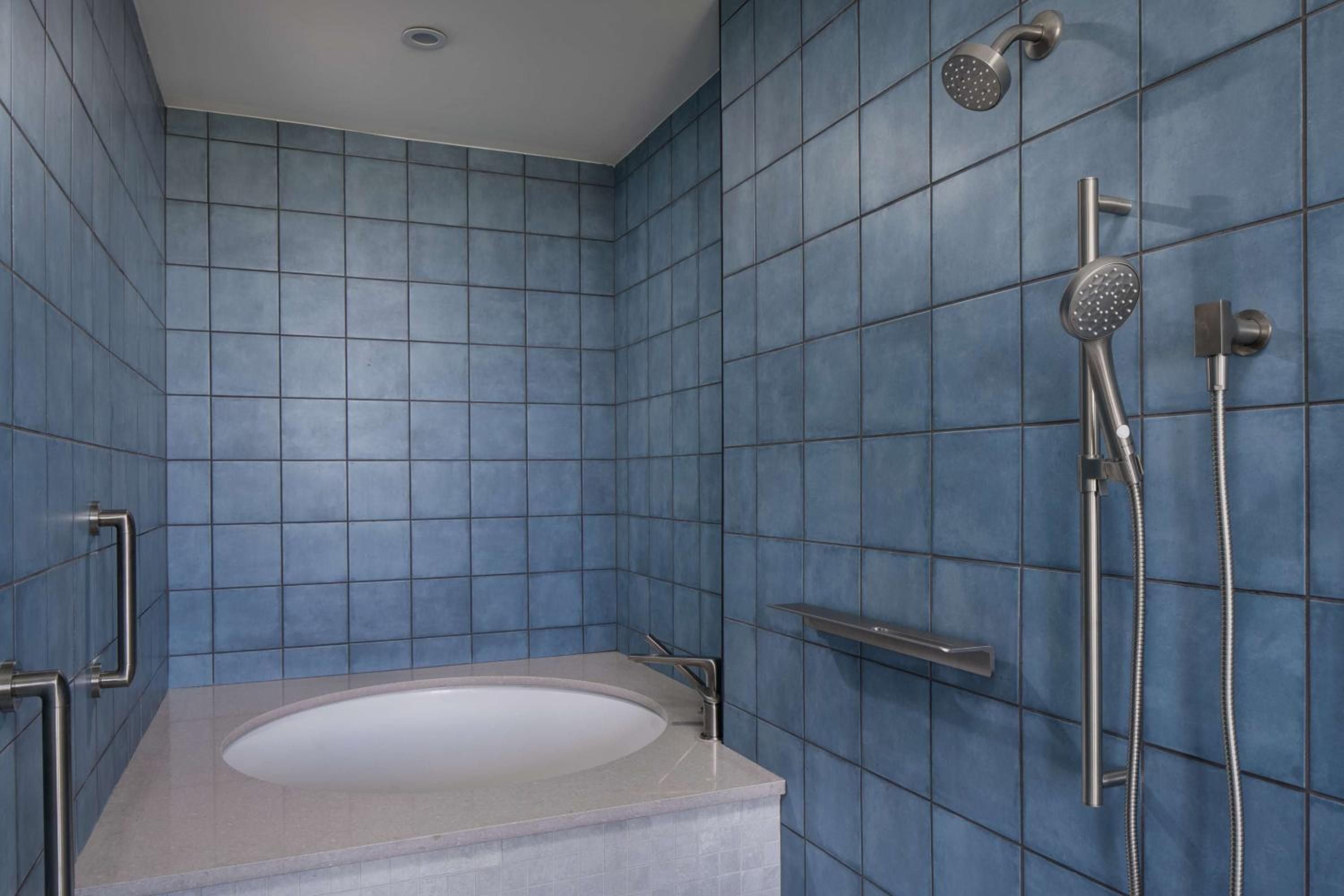 Sapphire-blue tiles create a serene spa-like atmosphere in this thoughtfully designed bathroom, where rainfall showers and handheld fixtures offer flexible bathing options.