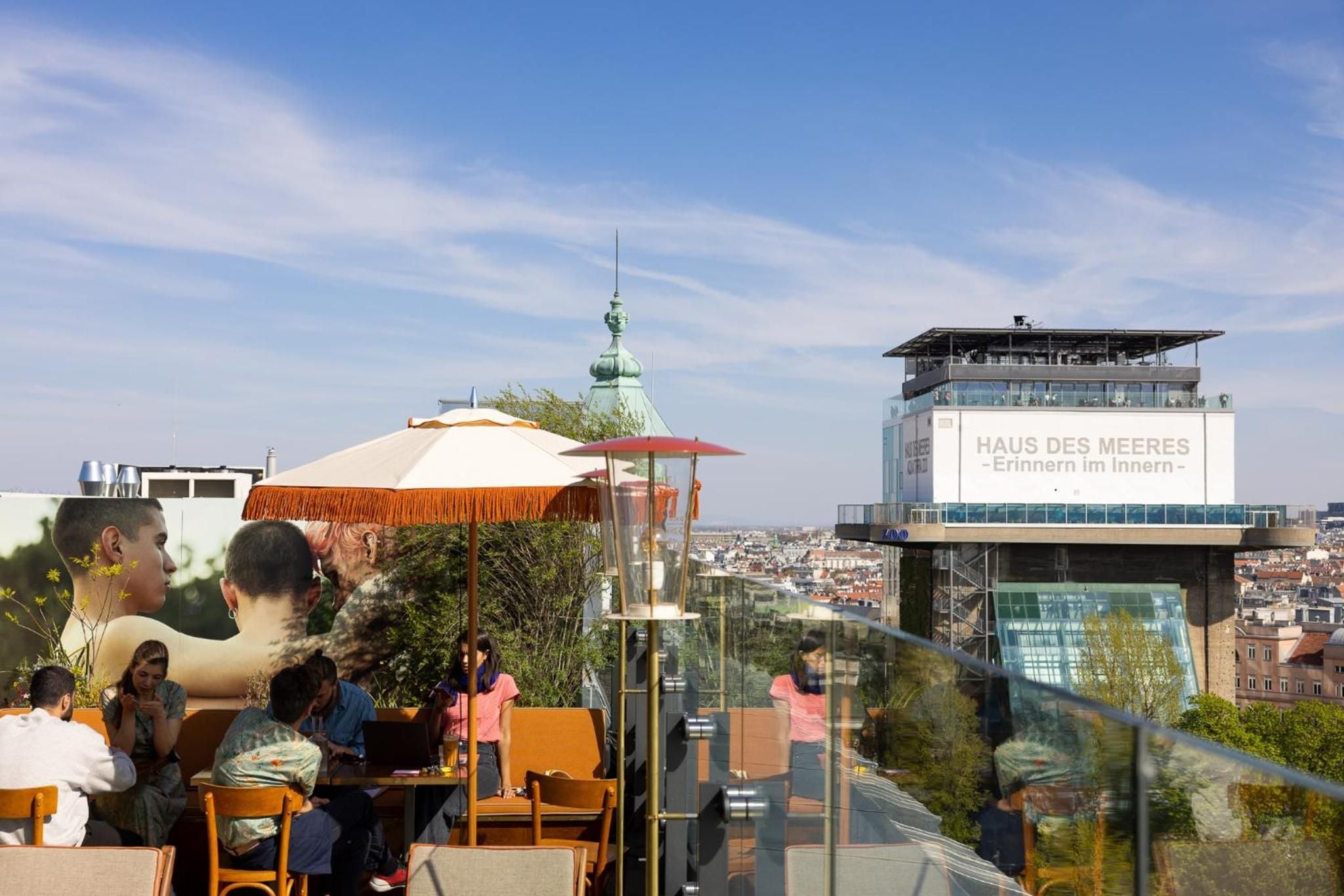 Orange parasols and vintage chairs create an intimate rooftop retreat where guests sip cocktails against Vienna's baroque skyline and the striking Haus des Meeres tower.