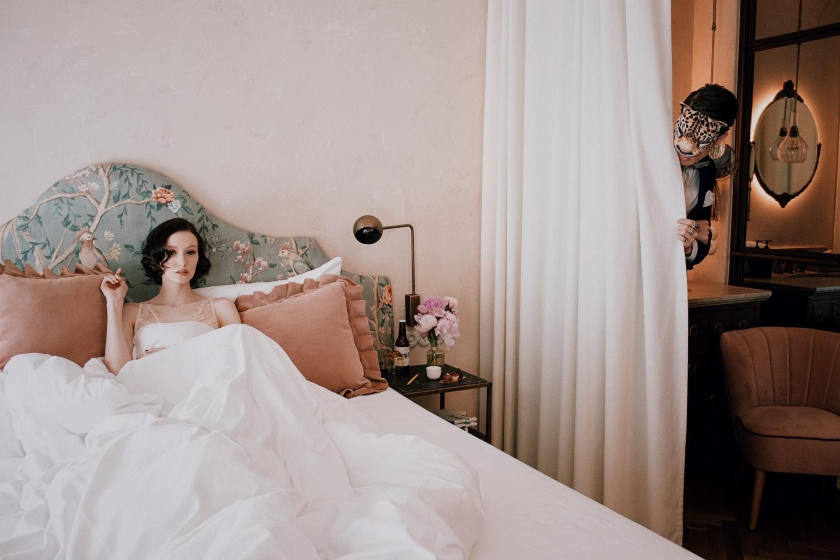 Floral headboards and ruffled coral pillows create an intimate boudoir atmosphere, while warm lamplight casts a golden glow across crisp white linens and thoughtful styling touches.