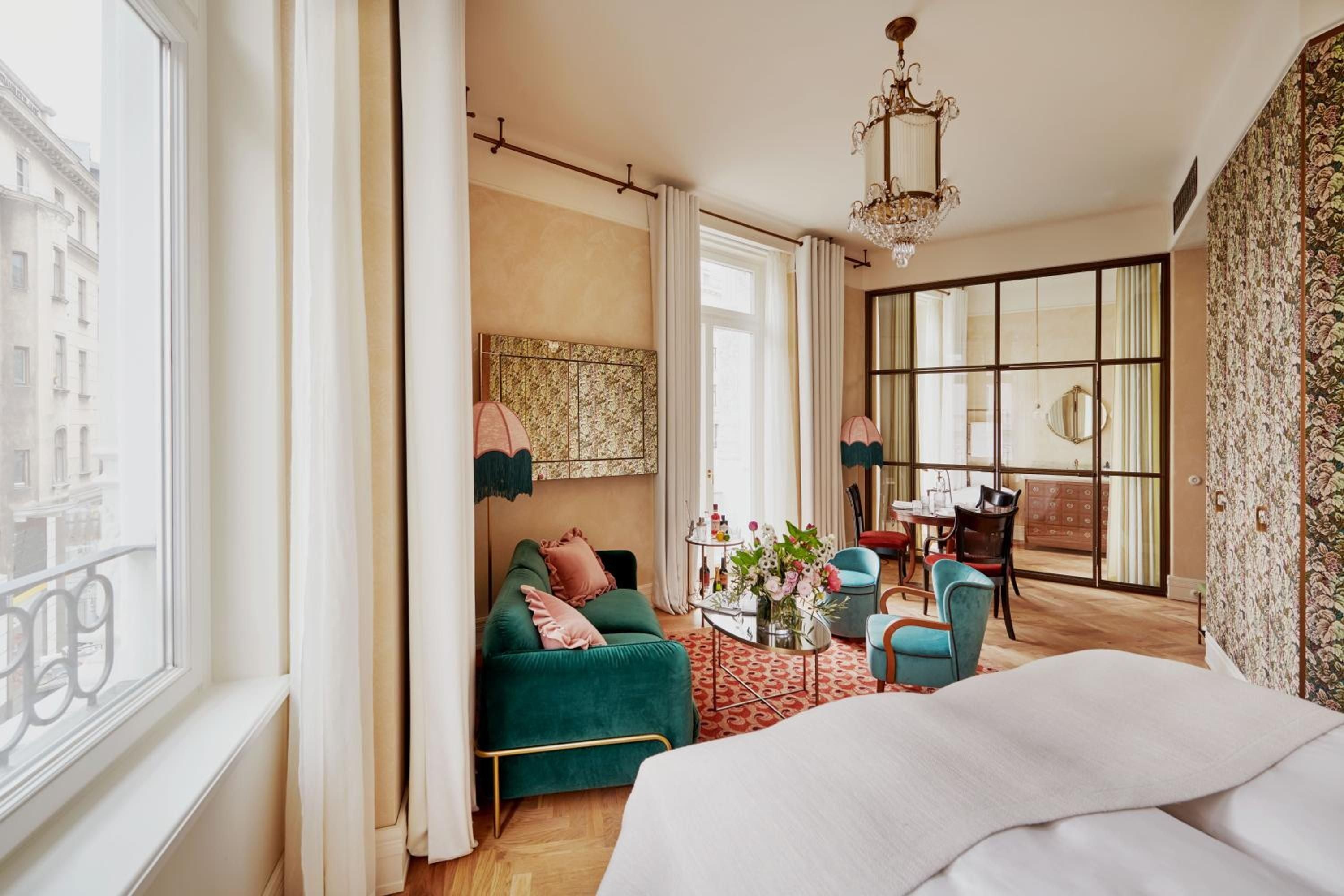 Emerald velvet seating and patterned wallpaper create an intimate sitting area, while mirrored closets reflect warm afternoon light streaming through tall windows.