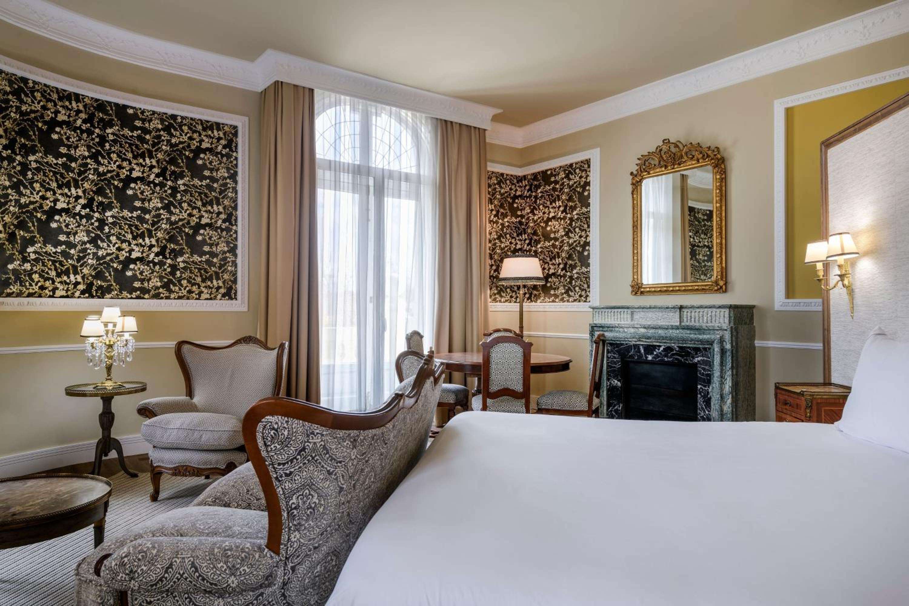 Gilded mirrors and dark floral wallpaper create an aristocratic ambiance in this sumptuous suite, where marble fireplace and crystal sconces evoke old-world Madrid grandeur.