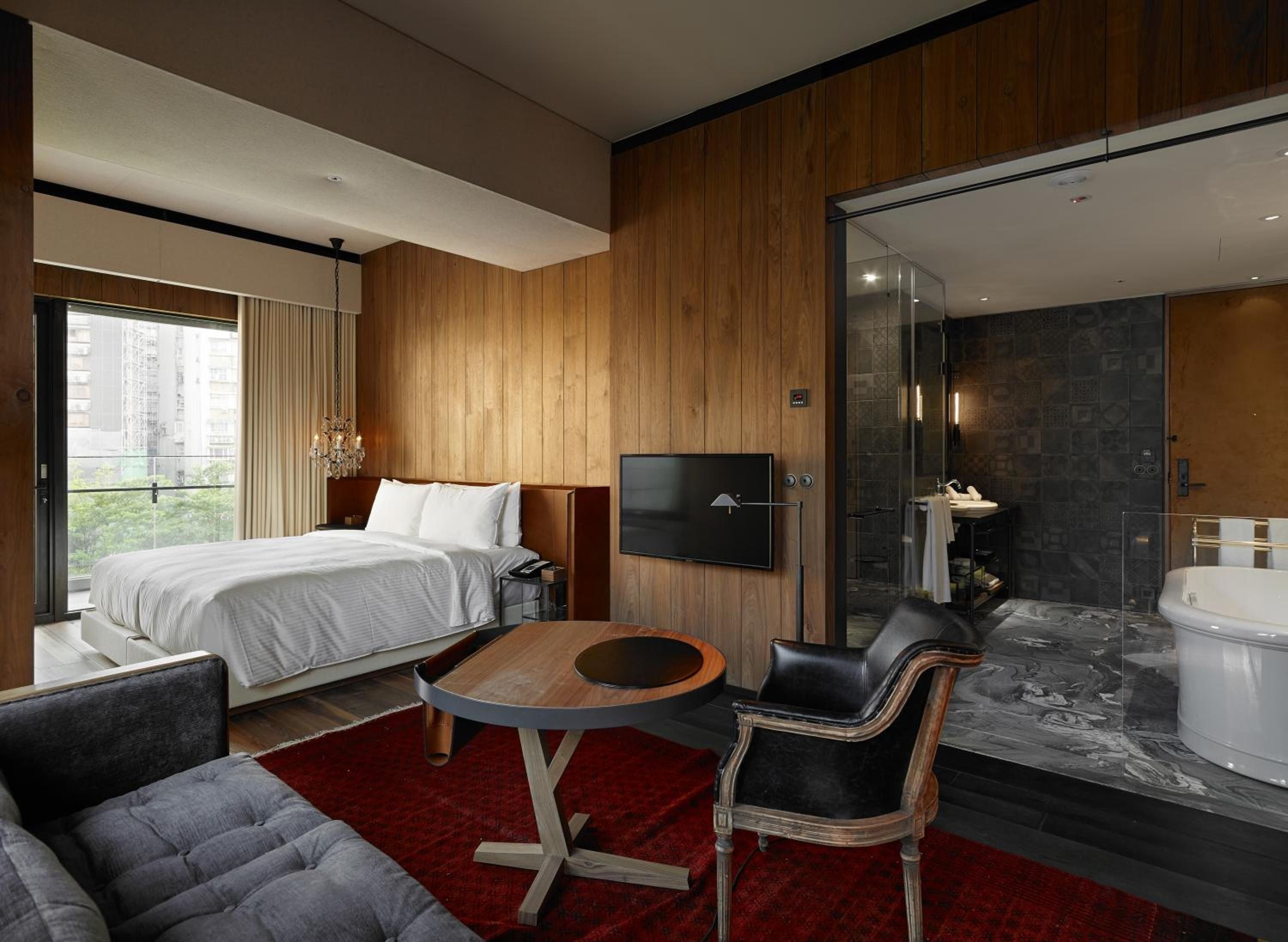 Warm wood paneling embraces this sophisticated suite where glass walls dissolve boundaries between sleeping and bathing spaces, creating an intimate urban sanctuary.