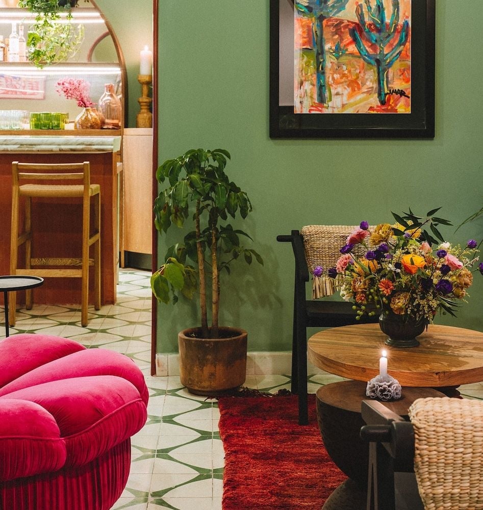 Sage-green walls frame a cozy corner where vibrant florals cascade from weathered wood tables, while soft candlelight dances across terra cotta tiles.