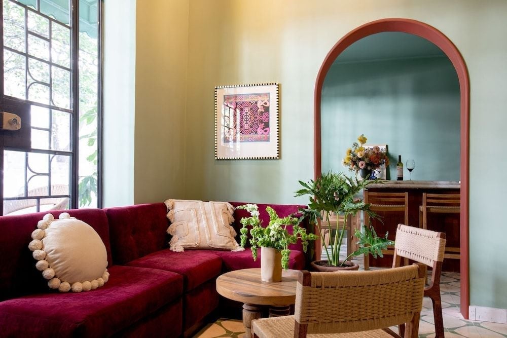 Burgundy velvet sectionals and woven chairs create intimate conversation nooks, while an arched doorway frames glimpses of the dining area beyond.