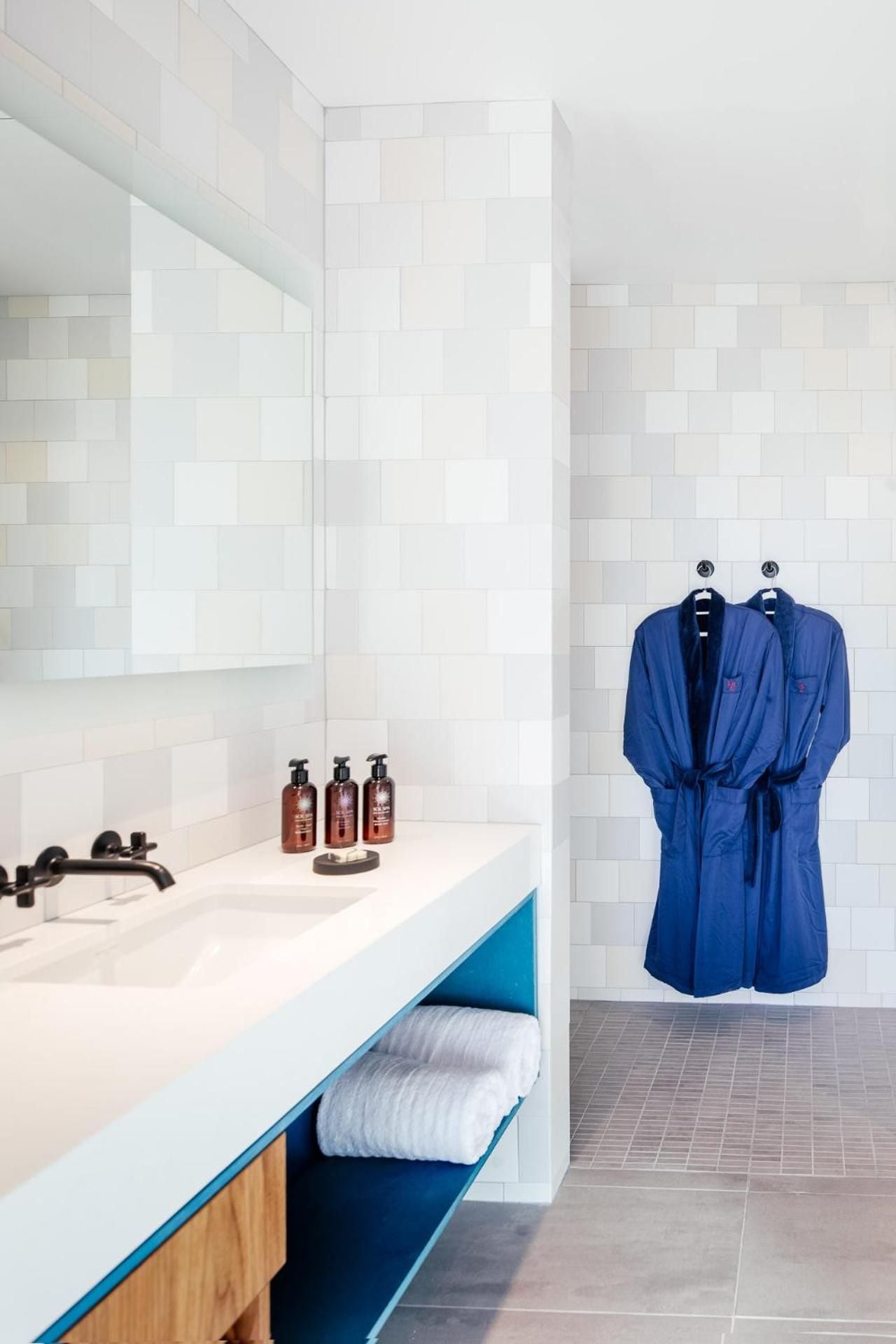 Crisp white subway tiles and a striking turquoise vanity create spa-like serenity, while plush blue robes await on sleek wall hooks in this thoughtfully appointed bathroom.