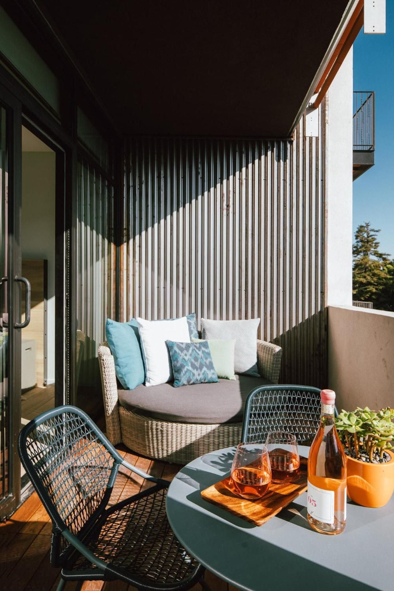 Vertical timber slats create intimate shadows on this thoughtfully appointed balcony, where wicker seating and rosé await golden hour moments above San Luis Obispo's rooftops.