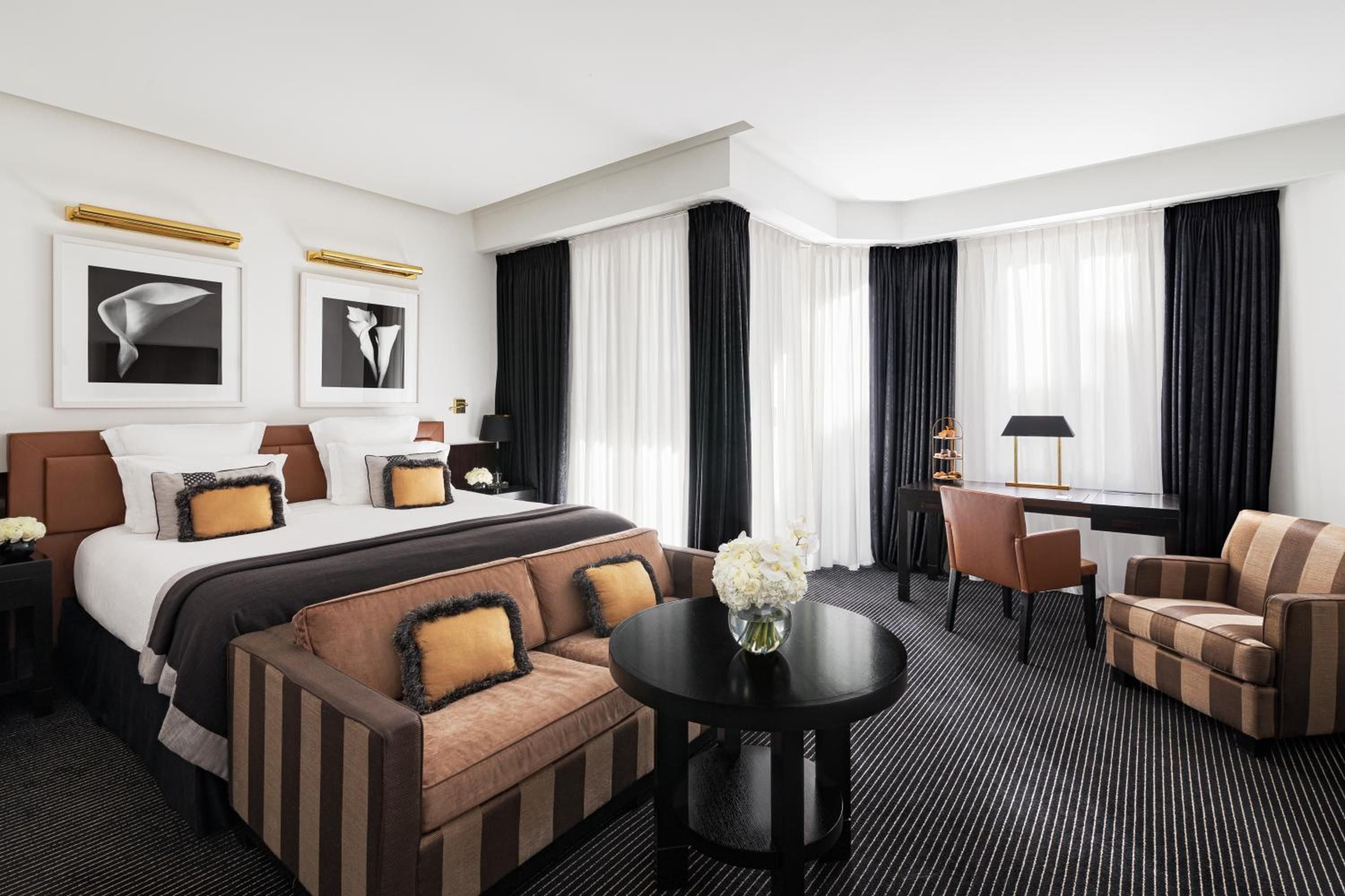 Cognac leather headboards and striped seating create intimate sophistication in this corner suite, where black and white photography adds artistic gravitas above plush bedding.