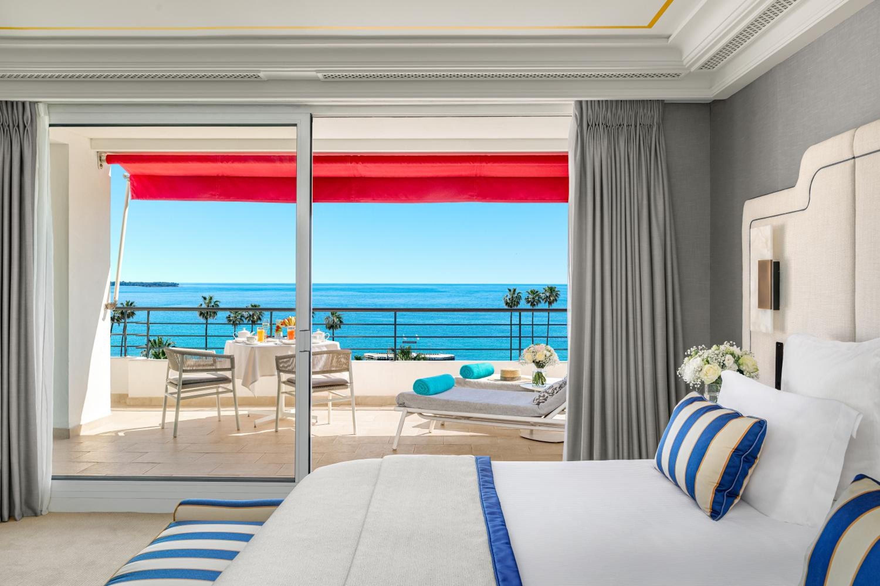 Crisp nautical stripes frame panoramic Croisette views from this elegant suite, where red awnings cast warm shadows over the sun-drenched Mediterranean terrace.