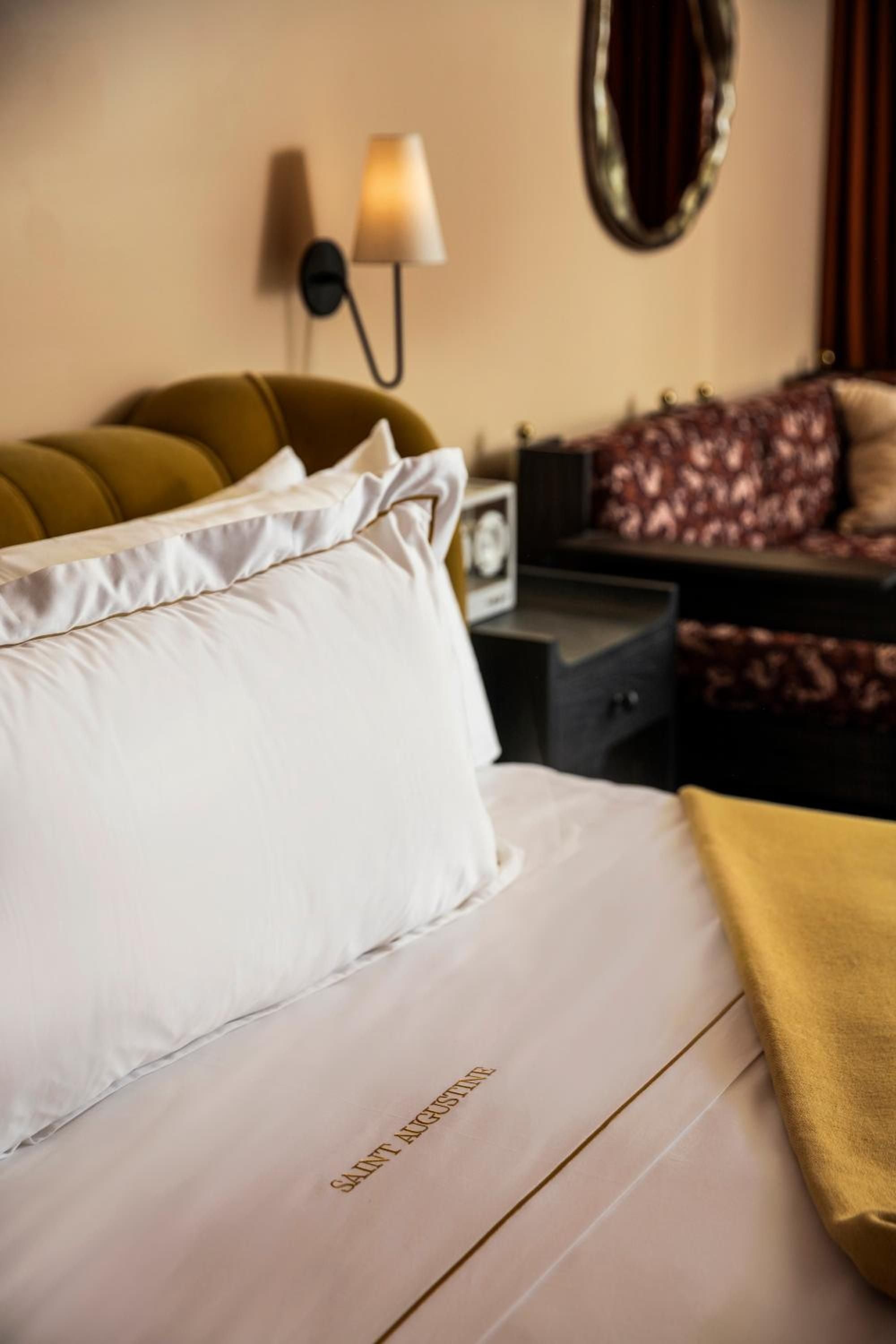Crisp white linens contrast beautifully with the mustard velvet headboard, while warm sconces cast an intimate glow across this thoughtfully appointed guest room.
